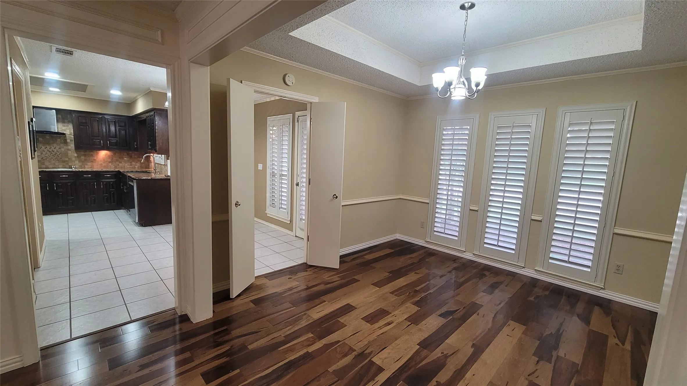 Dining area featuring wood-finish flooring, tray ceiling, crown molding, chair rail trim, and plantation shutters
