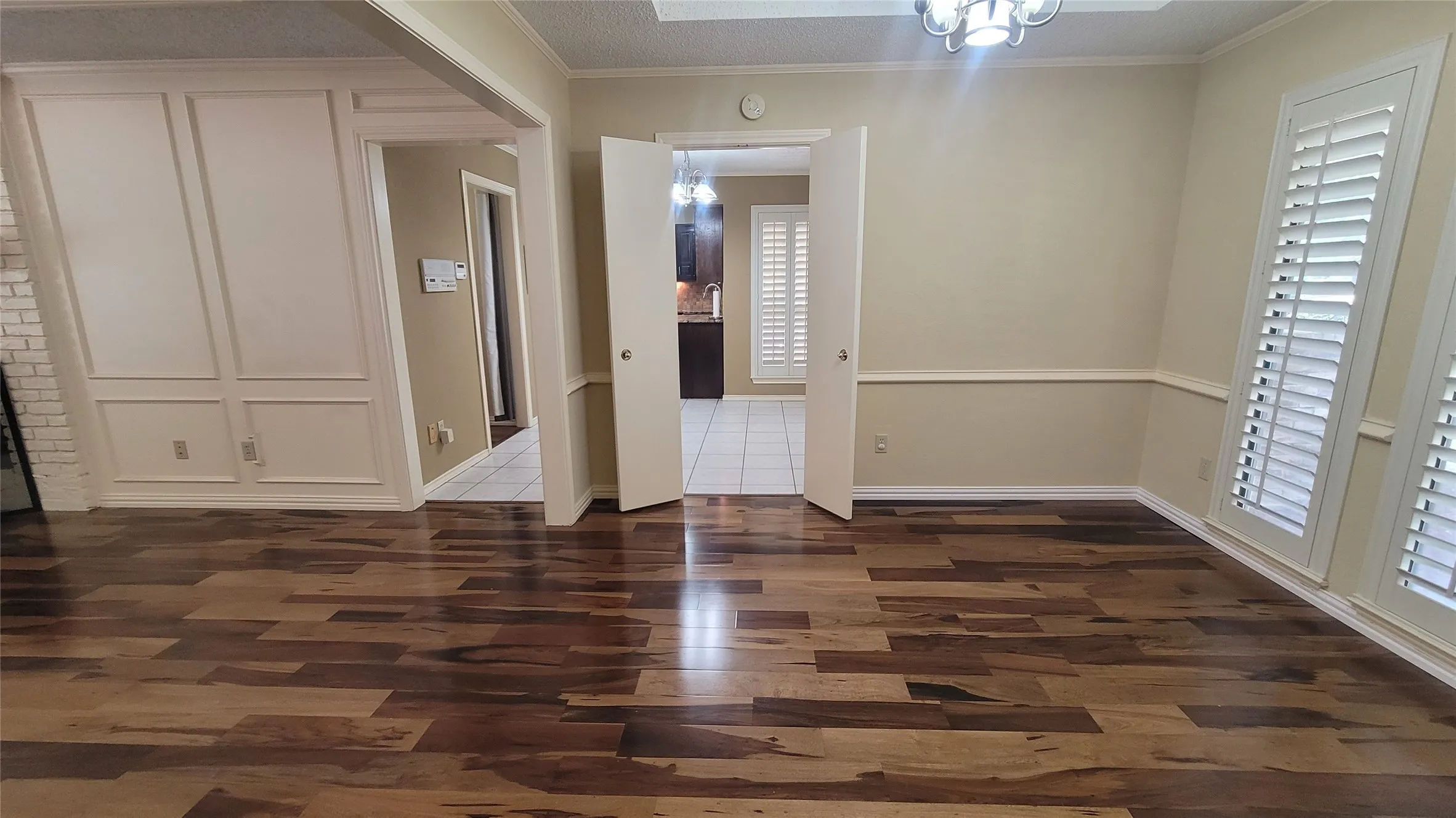 Wood-finish flooring, wainscoting detail, plantation shutters, and multi-panel interior doors