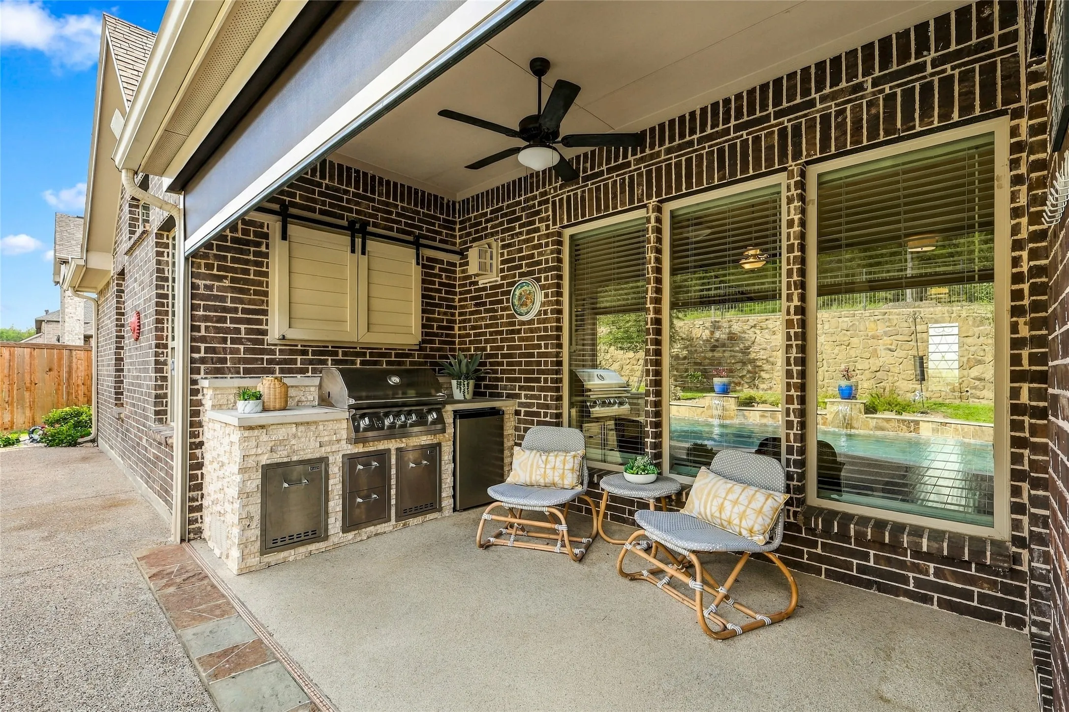 Covered patio featuring brick masonry, a built-in outdoor kitchen with stainless steel appliances, stone-veneer cabinetry, ceiling fan, and remote contolled patio screen