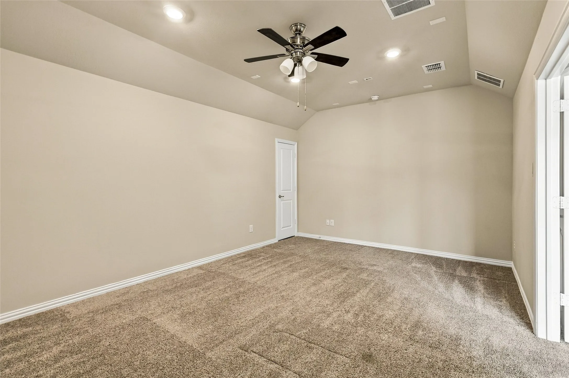 Interior space featuring vaulted ceilings, neutral wall tones, textured carpeting, a multi-blade ceiling fan with integrated lighting, and recessed overhead illumination