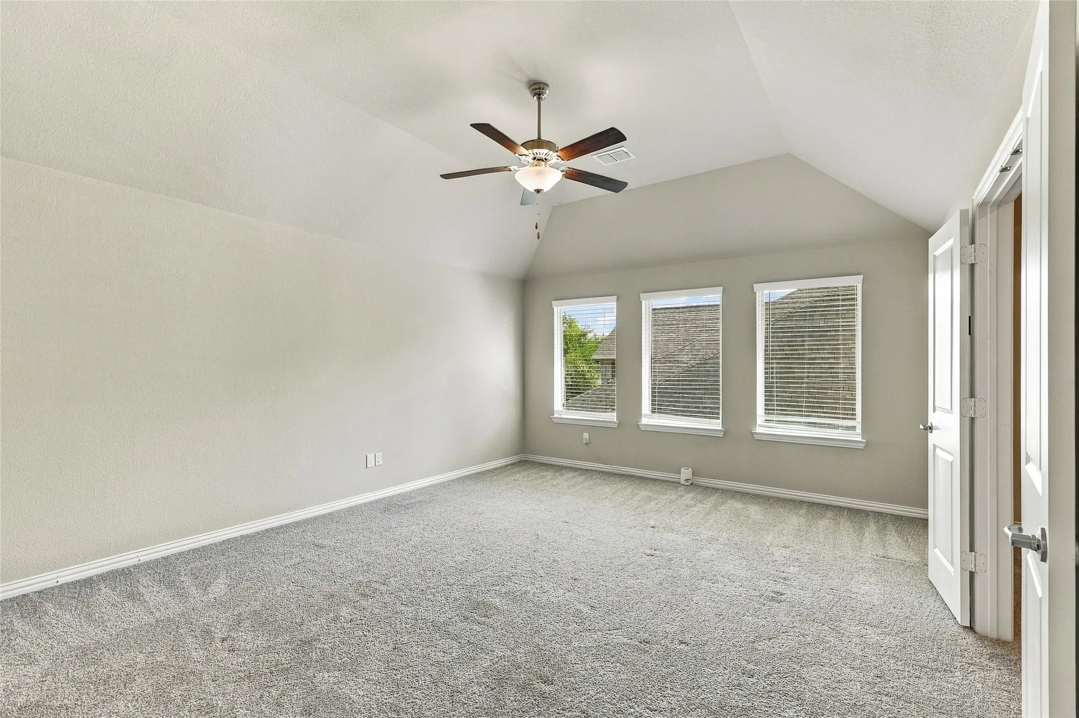 Vaulted ceiling featuring a central multi-blade ceiling fan with integrated light fixture, neutral wall palette, carpeting, and three windows