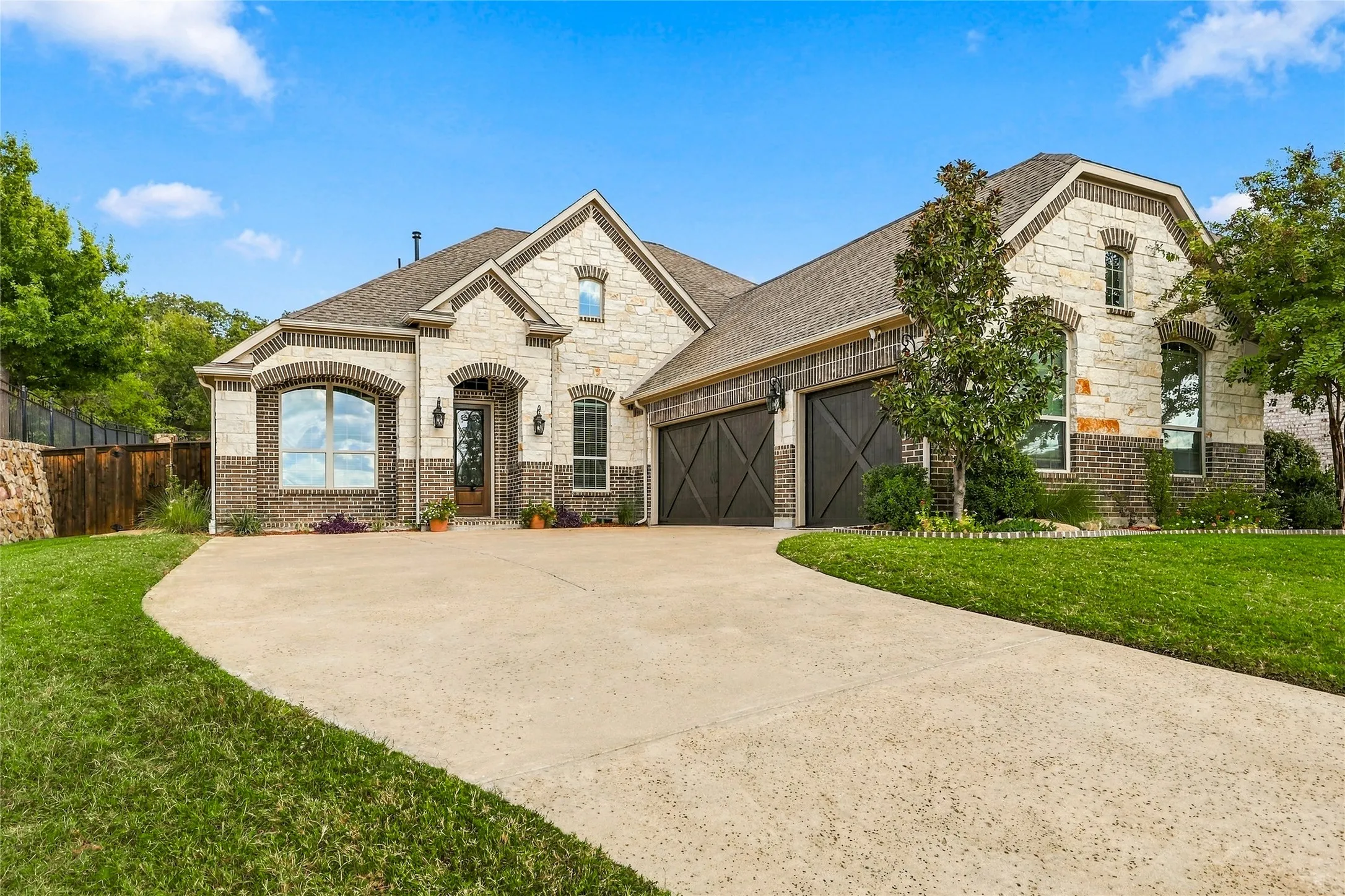 Multi-gabled exterior featuring stone and brick masonry, arch-top entryway, and two-car garage with decorative cross-buck detailing