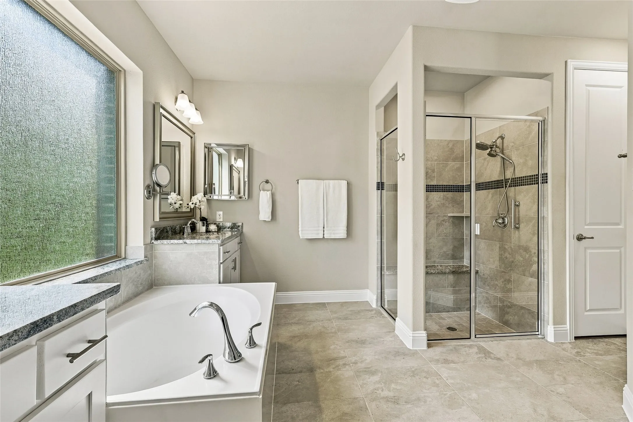 Bathroom featuring a soaking tub with chrome fixtures, a separate glass-enclosed shower with tile surround, stone-top vanity, and large-format tile flooring