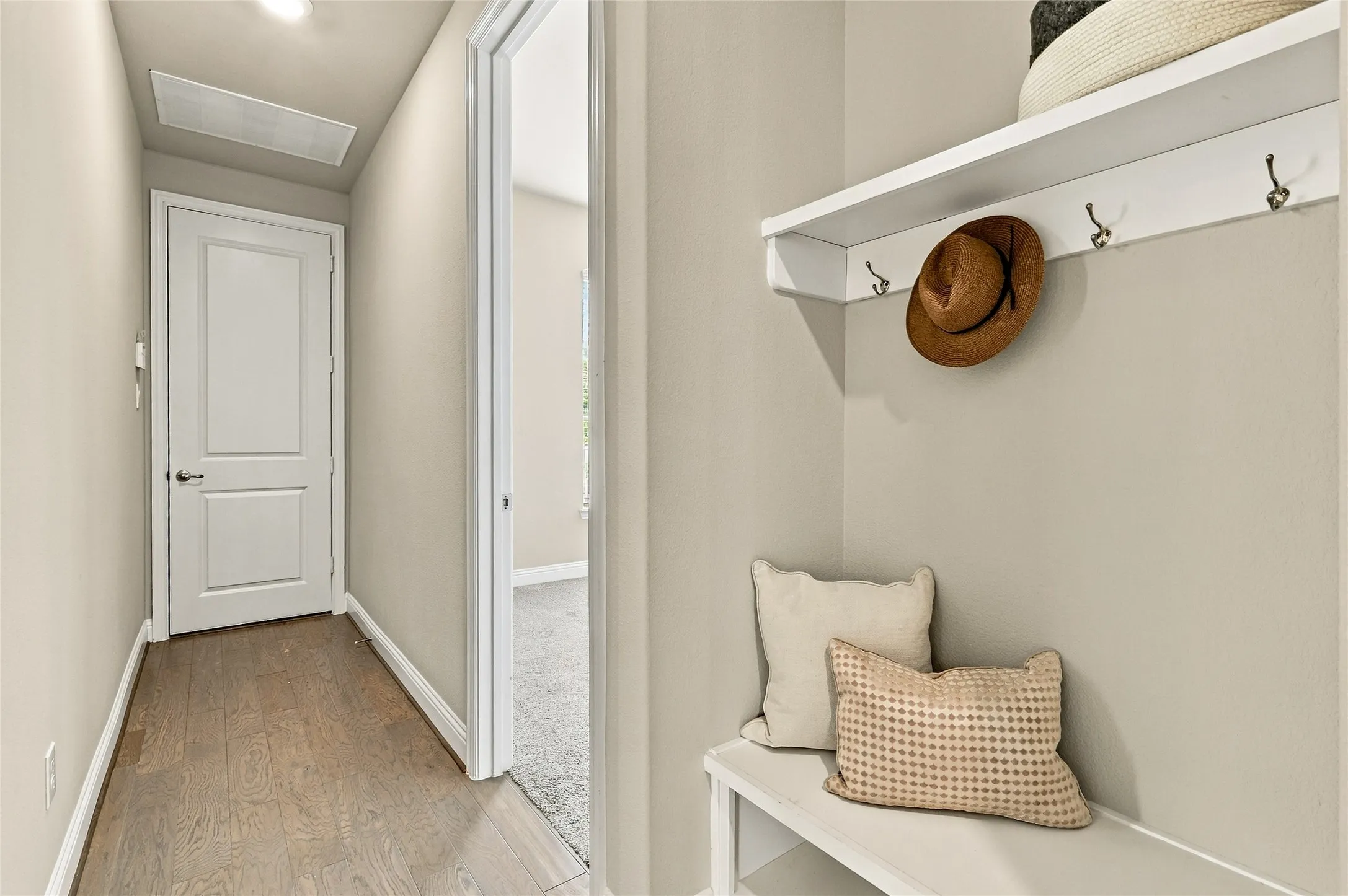 Built-in wall-mounted shelving unit with integrated coat hooks, recessed ceiling lighting, wood-finish flooring, and a solid-core panel door