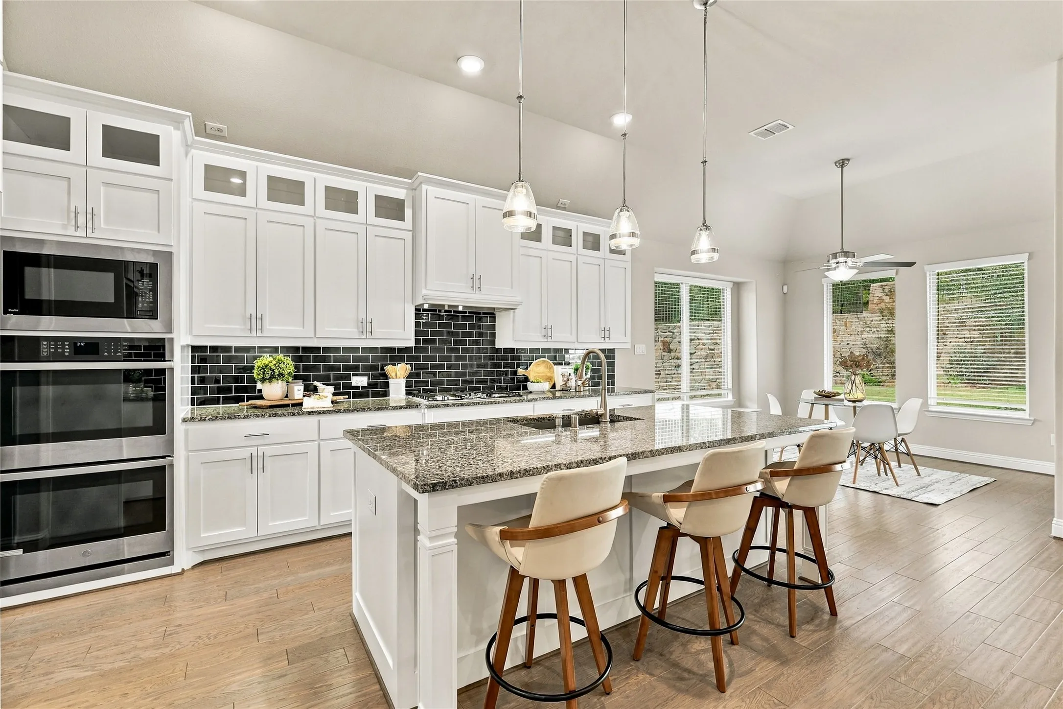 Kitchen featuring white cabinetry, stone countertops, a center island with a built-in sink, glass-tile backsplash, and wood-finish flooring