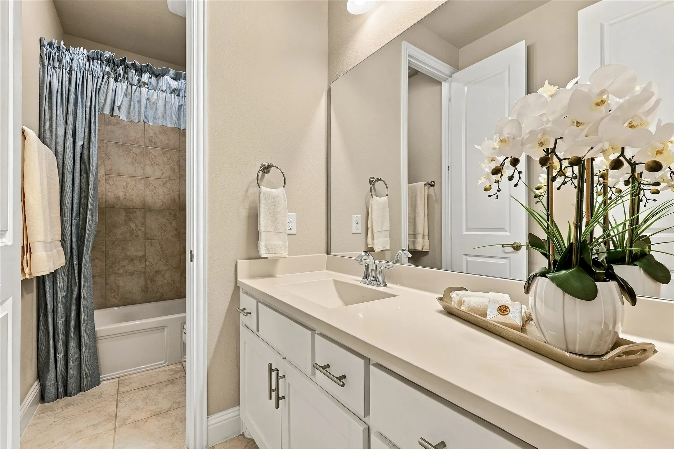 Bathroom featuring a vanity with a solid-surface countertop, an integrated sink, white cabinetry with brushed-metal pulls, and a full-width mirror