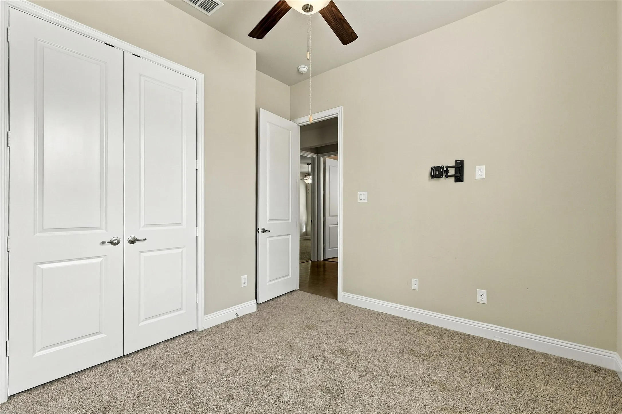 Neutral wall tones, wall-to-wall carpeting, ceiling fan with integrated lighting, two-panel interior doors, and a wall-mounted television bracket