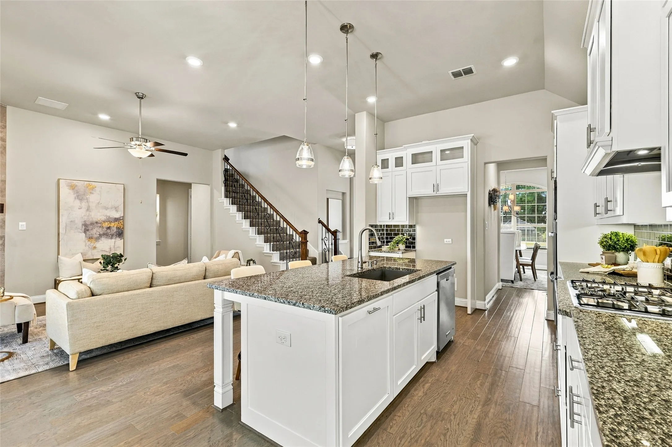 Kitchen featuring white shaker-style cabinetry, stone countertops, stainless steel appliances, wood-finish flooring, and pendant lighting