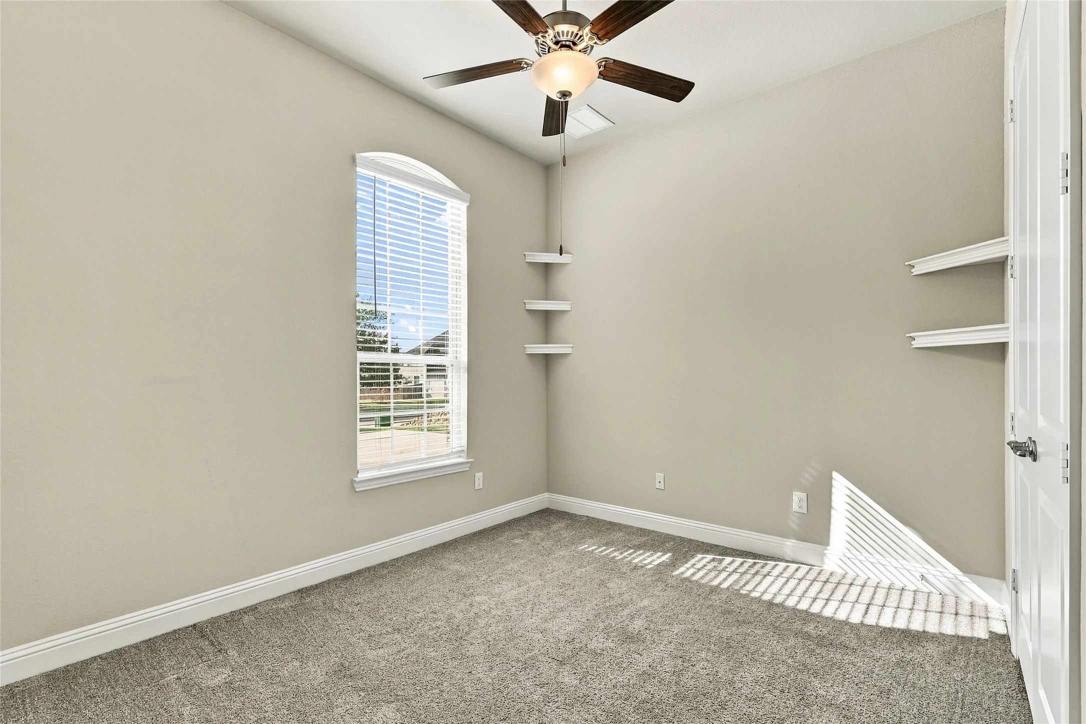 Room featuring an arched window, carpeted flooring, a ceiling fan with integrated lighting, and multiple built-in wall-mounted shelves