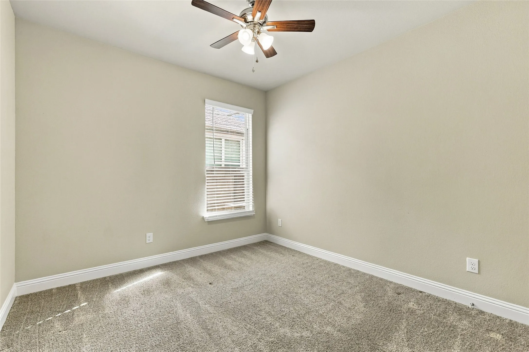 Neutral-toned interior featuring wall-to-wall carpeting, a multi-blade ceiling fan with integrated lighting, and a single-pane window with horizontal blinds