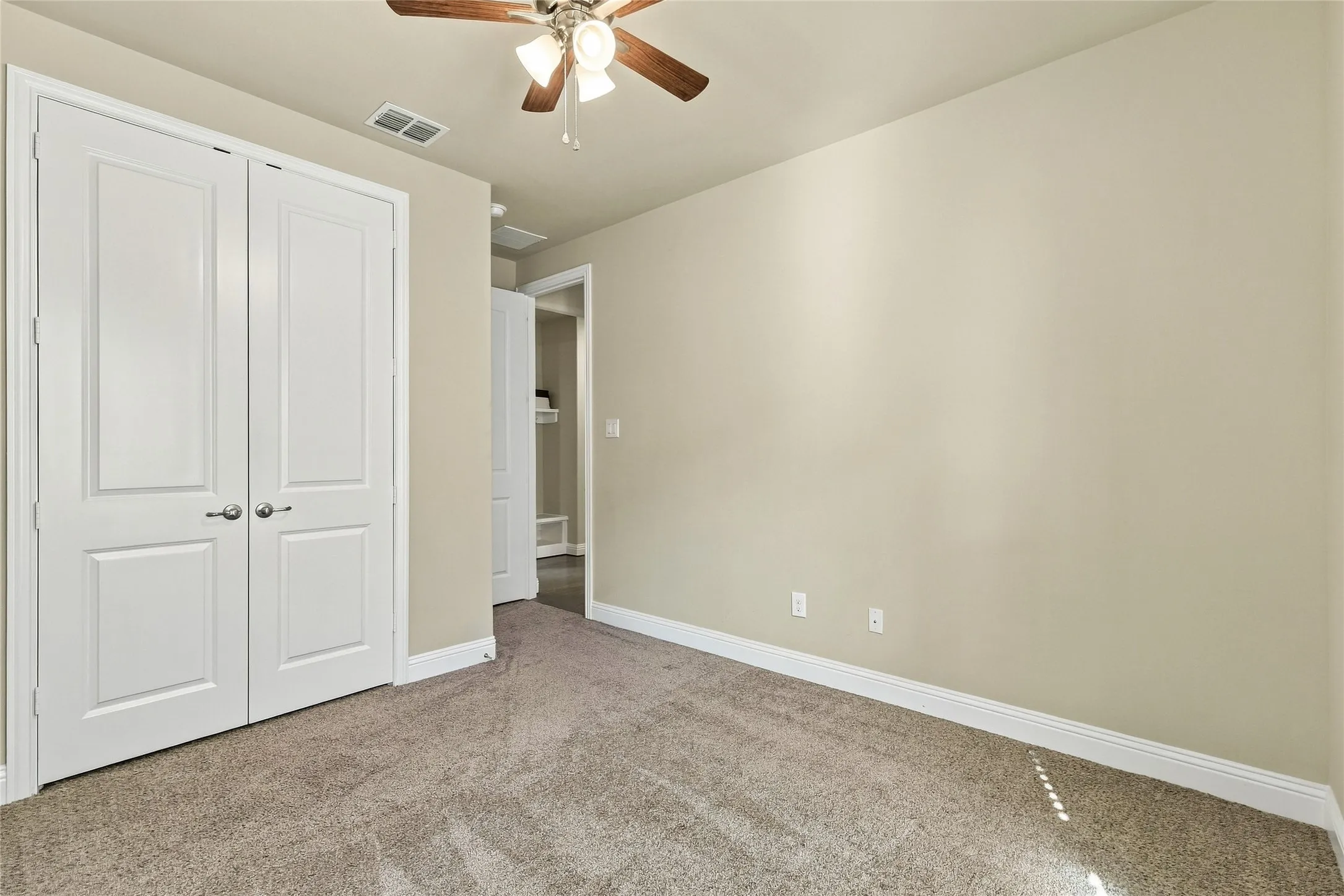 Neutral-toned walls, carpeted flooring, ceiling fan with integrated lighting, and double-panel closet doors