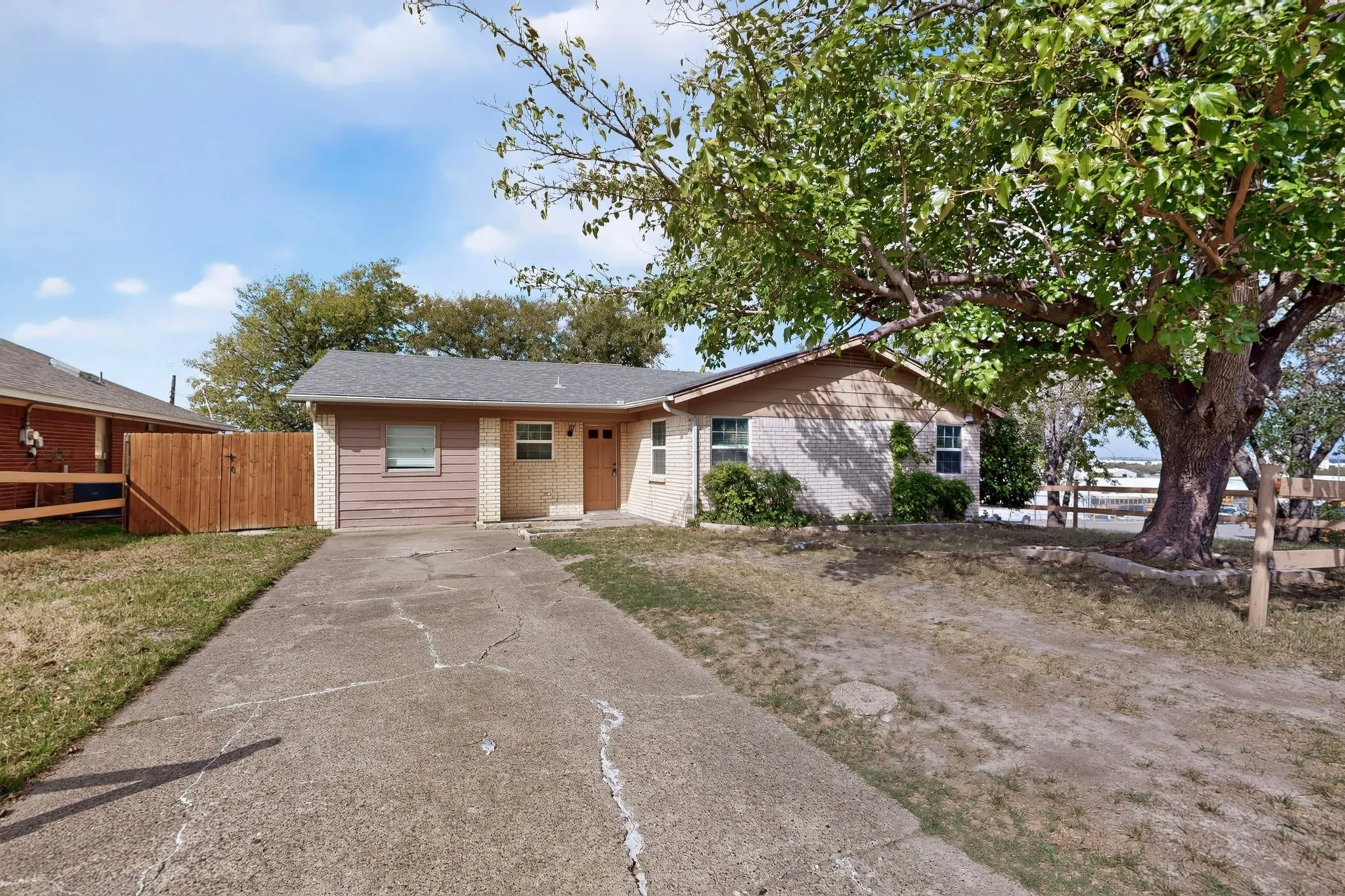 Single-story residence featuring light-colored masonry, horizontal siding, a concrete driveway, and a wooden perimeter fence