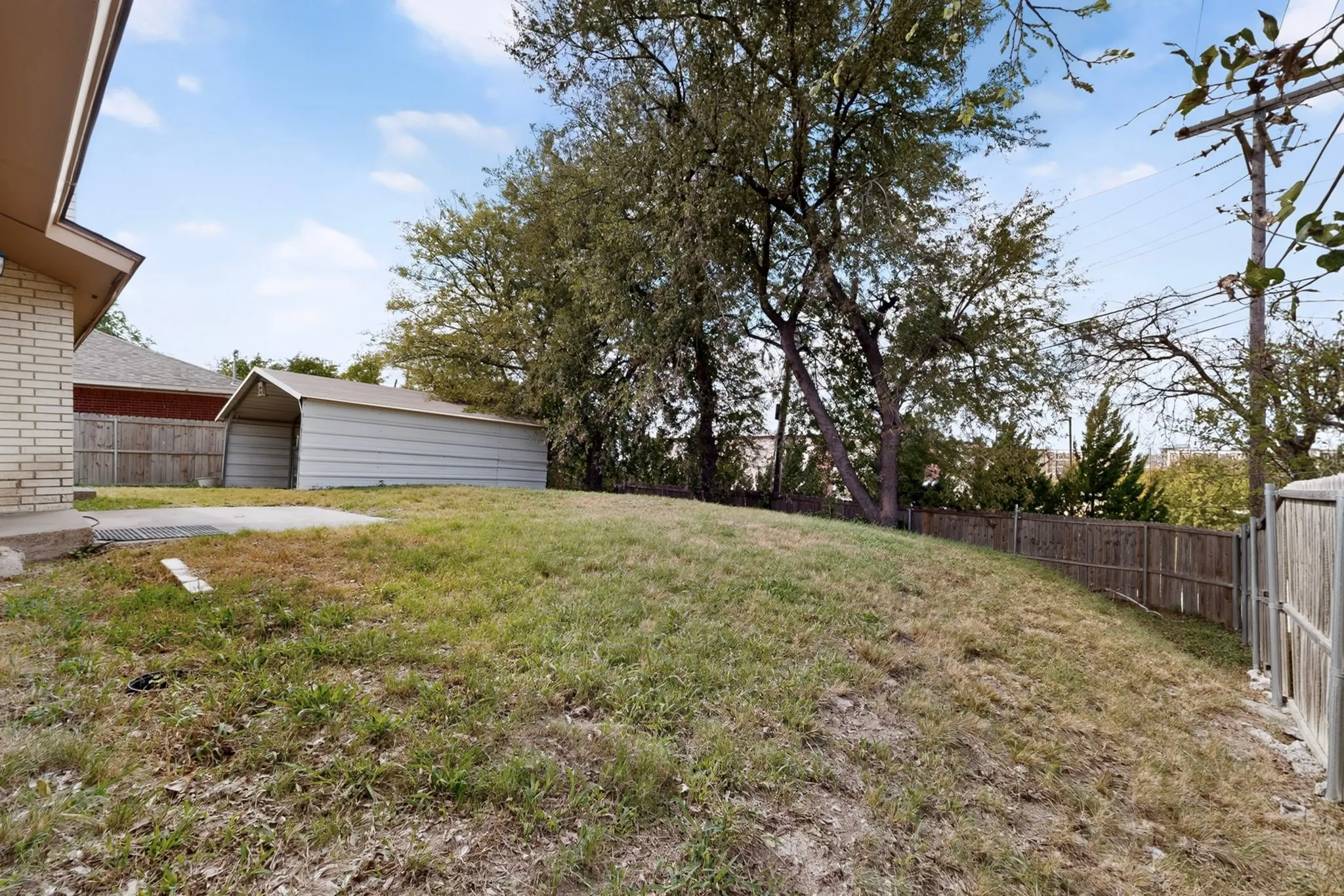 Backyard featuring a grass lawn, mature trees, metal storage structure, and wood privacy fencing