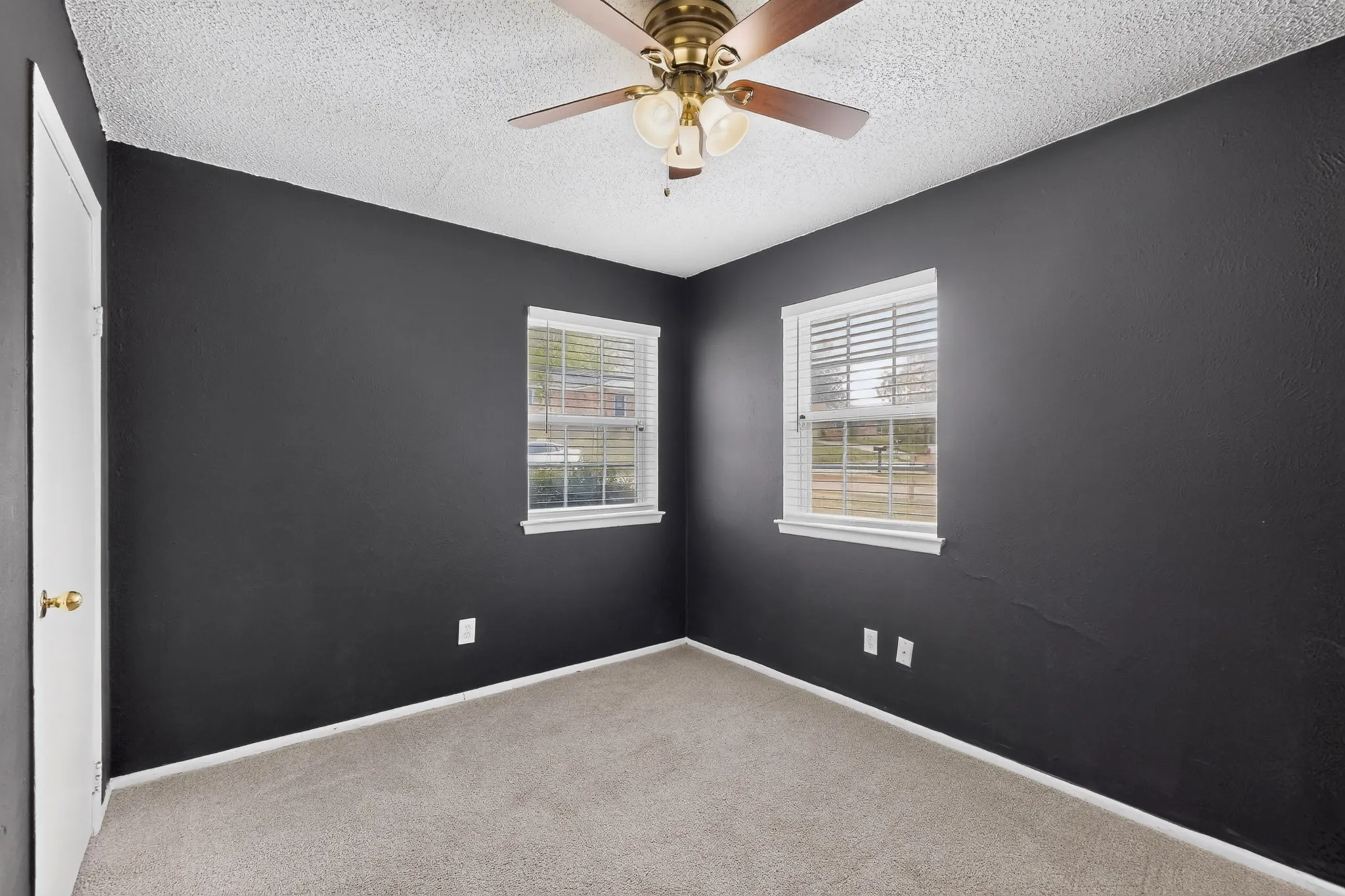 Room featuring high-contrast charcoal walls, neutral carpeting, a central ceiling fan with integrated lighting, and dual windows with built-in blinds