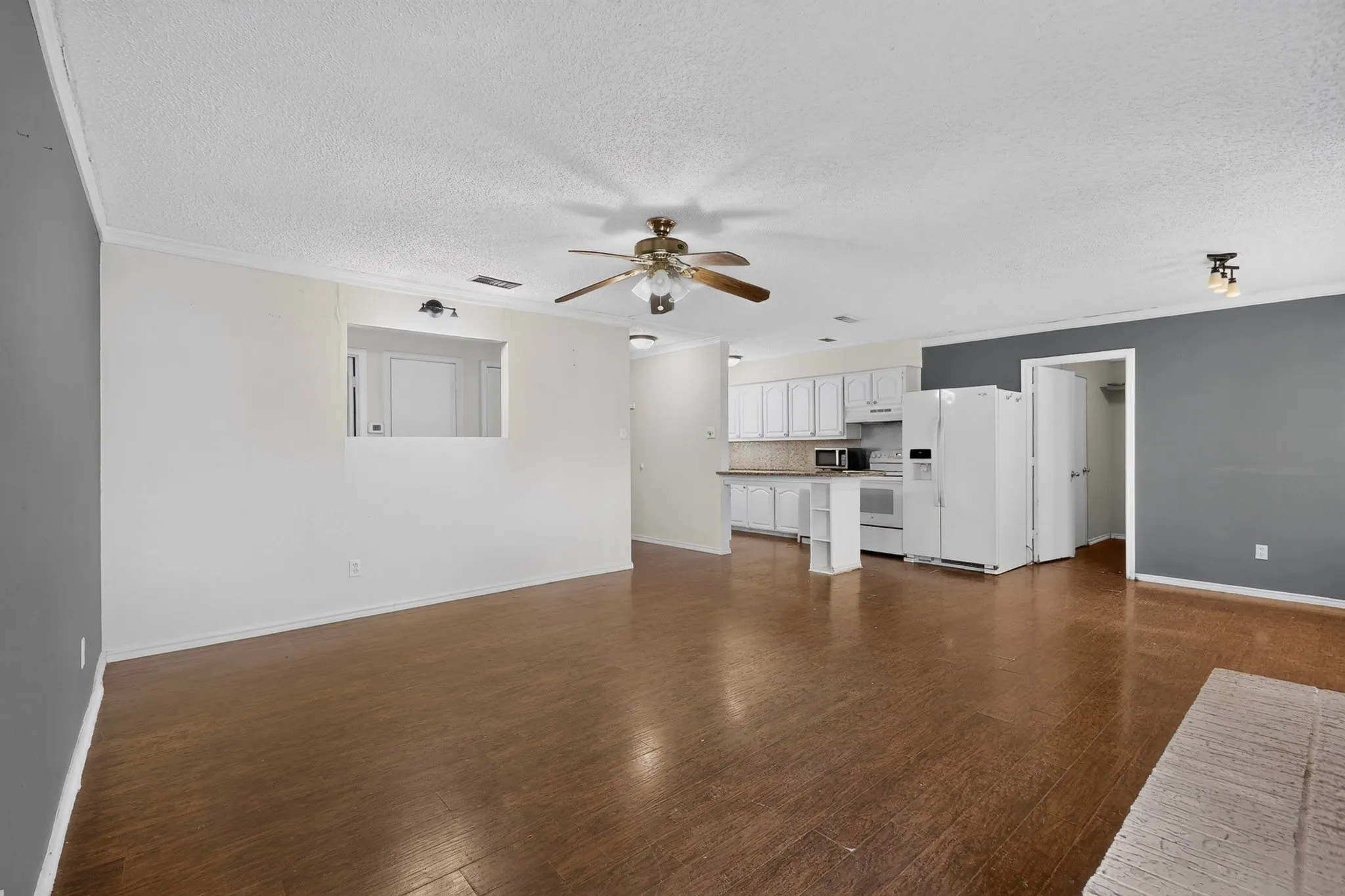 Open-concept interior featuring wood-finish flooring, a kitchen breakfast bar, white cabinetry, and a ceiling fan with integrated lighting