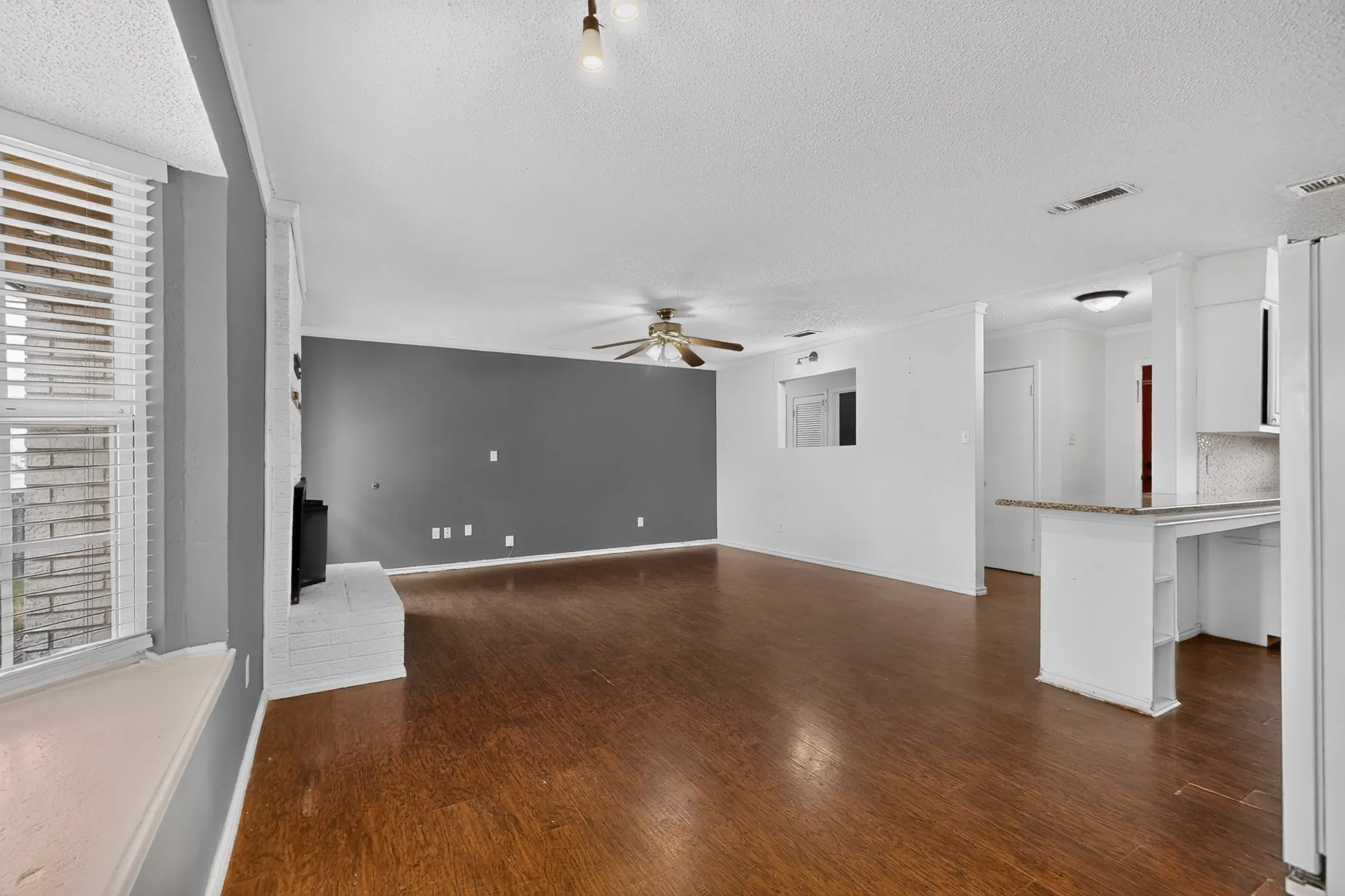 Open-concept interior featuring wood-finish flooring, a white painted brick fireplace, a built-in kitchen breakfast bar with stone-surface countertop, and a window seat