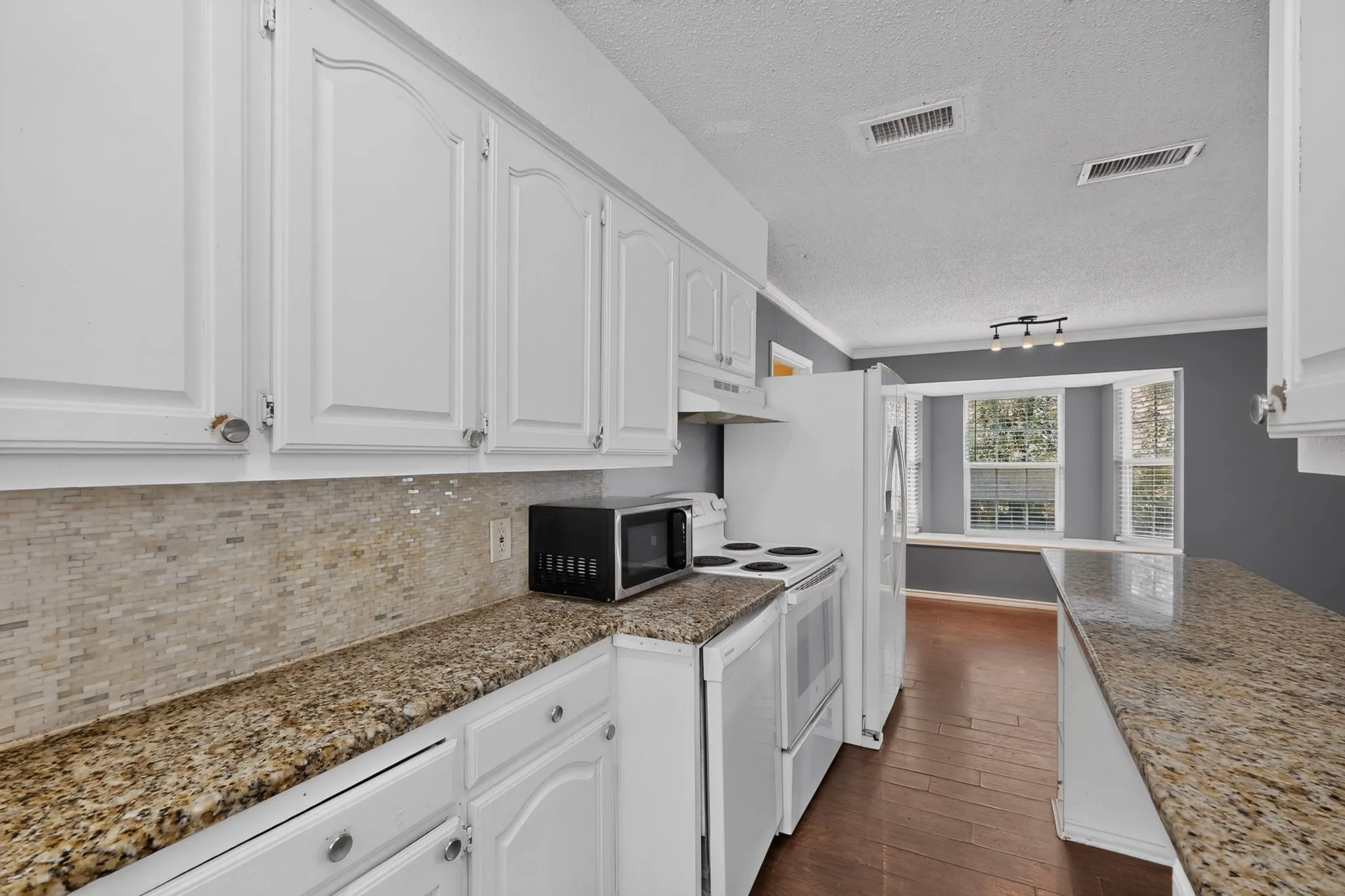Kitchen featuring white cabinetry, stone-finish countertops, textured stone backsplash, wood-finish flooring, and a bay window