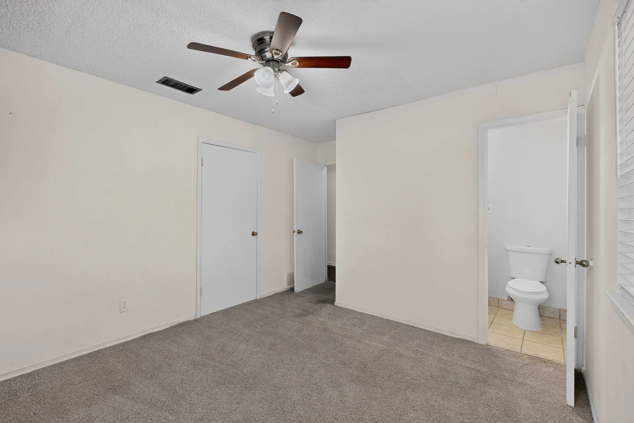 Interior space featuring neutral wall tones, wall-to-wall carpeting, ceiling fan with integrated lighting, and a private restroom with tile flooring