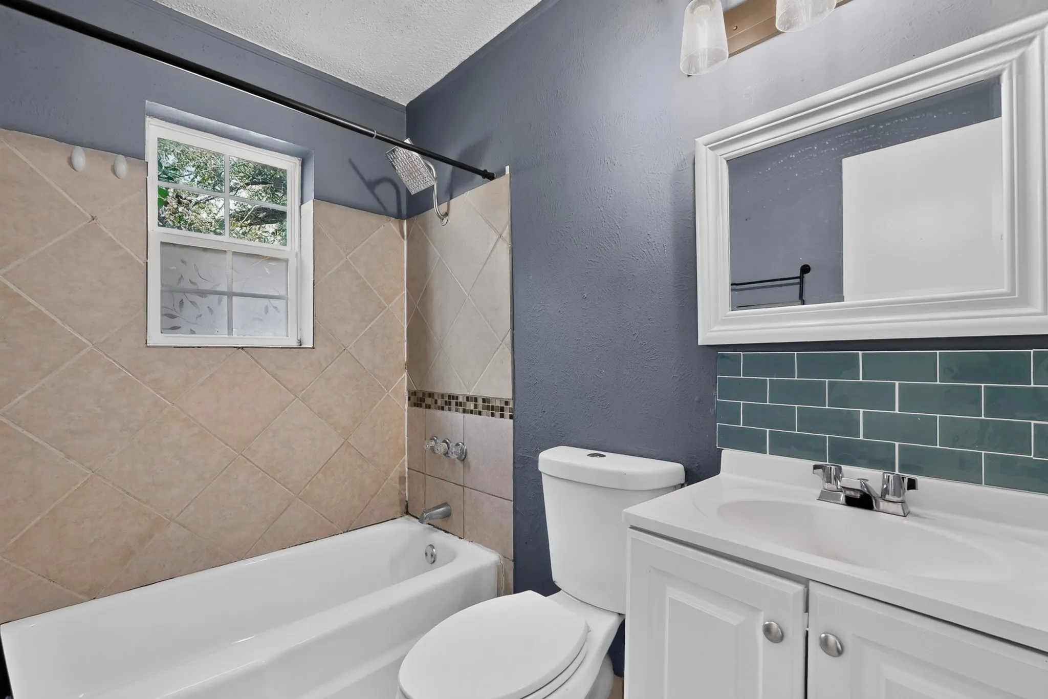 Bathroom featuring a white vanity with an integrated sink, teal subway tile backsplash, white framed wall mirror, and tub-shower combination with diagonal wall tiling