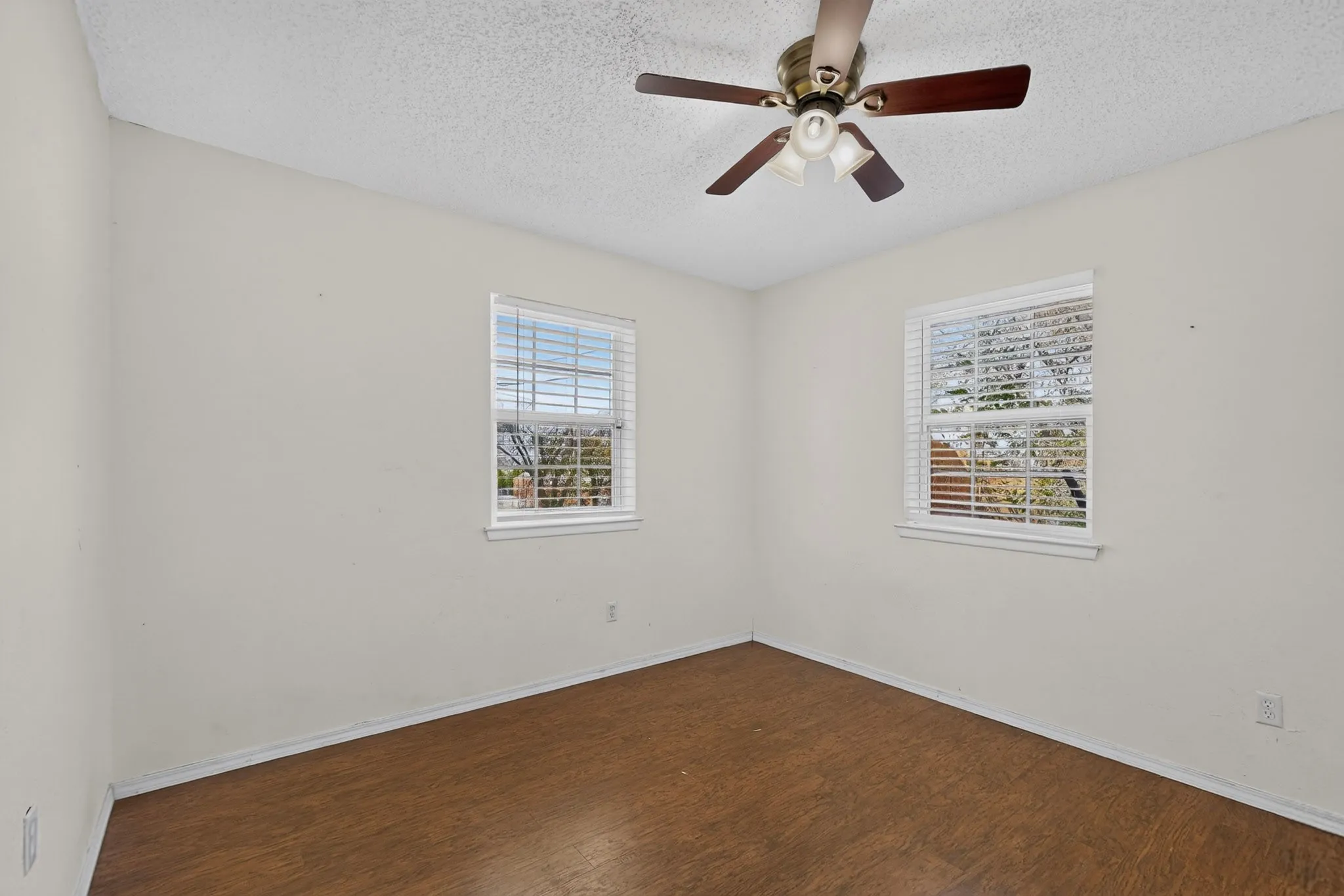 Room featuring wood-finish flooring, two windows with horizontal blinds, and a ceiling fan with integrated light fixture