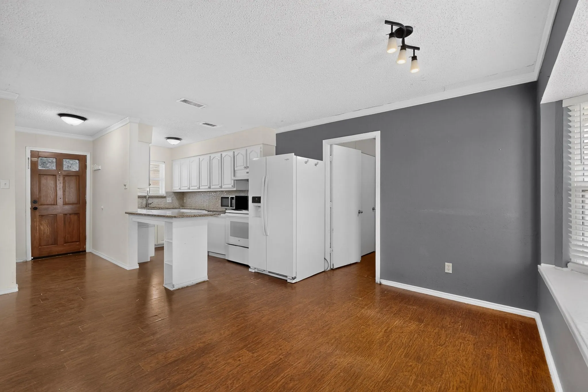 Kitchen area featuring white cabinetry, a peninsula with stone-finish countertop, wood-finish flooring, and a solid wood front entry door
