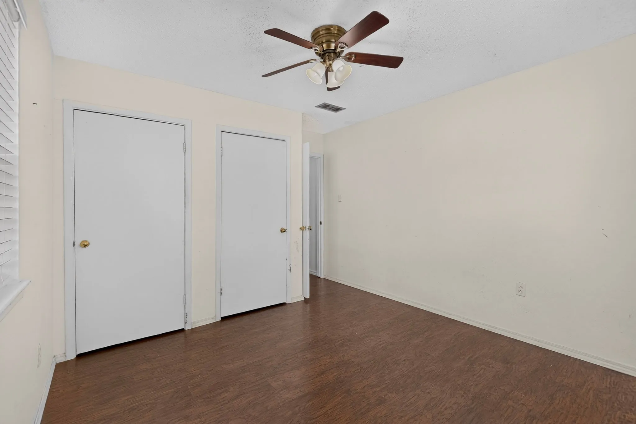 Room featuring wood-finish flooring, two sets of solid-core doors, and a ceiling-mounted light fixture with a fan