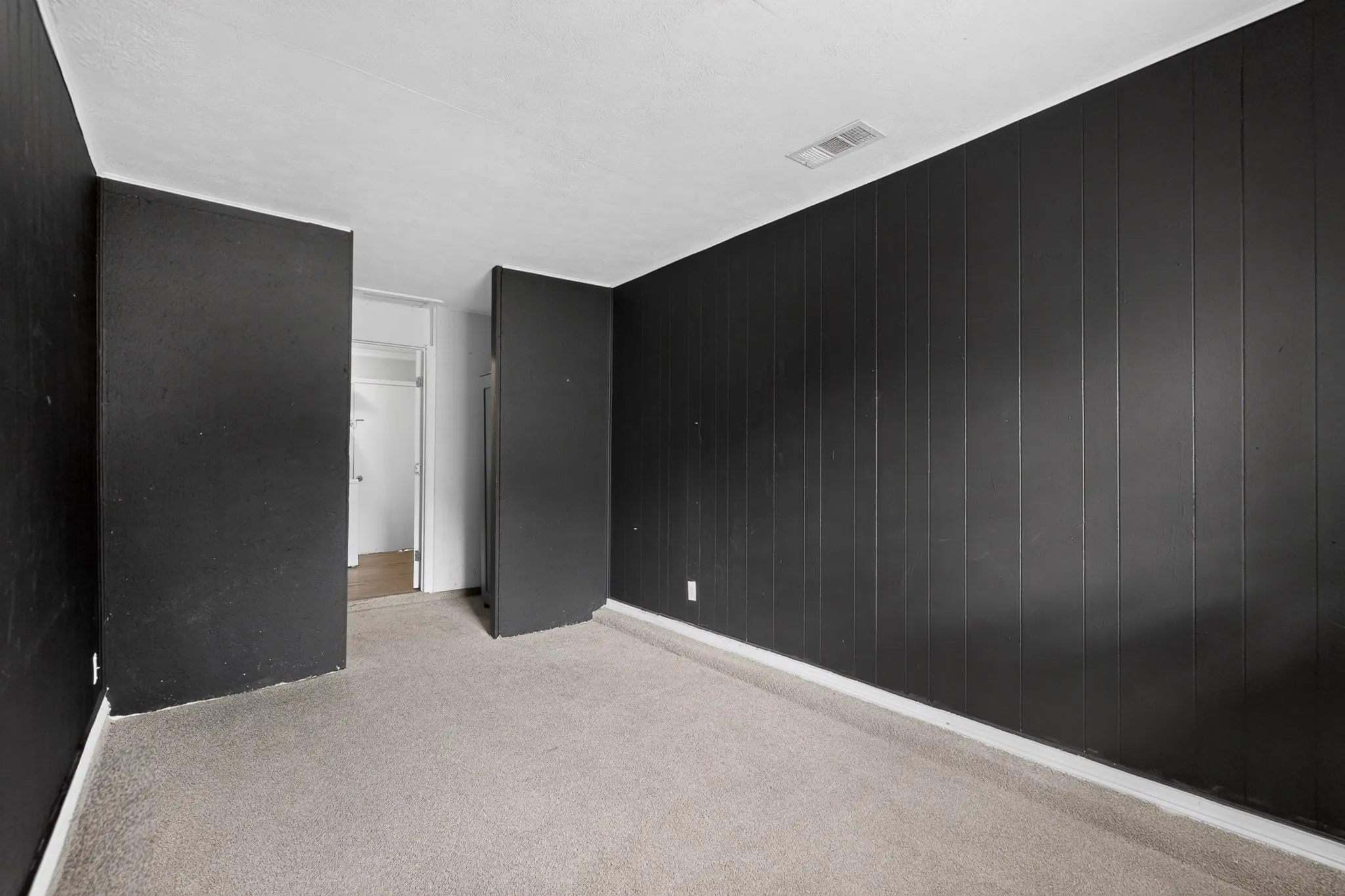 Interior space featuring vertical wood-paneled walls finished in matte black and neutral-toned wall-to-wall carpeting