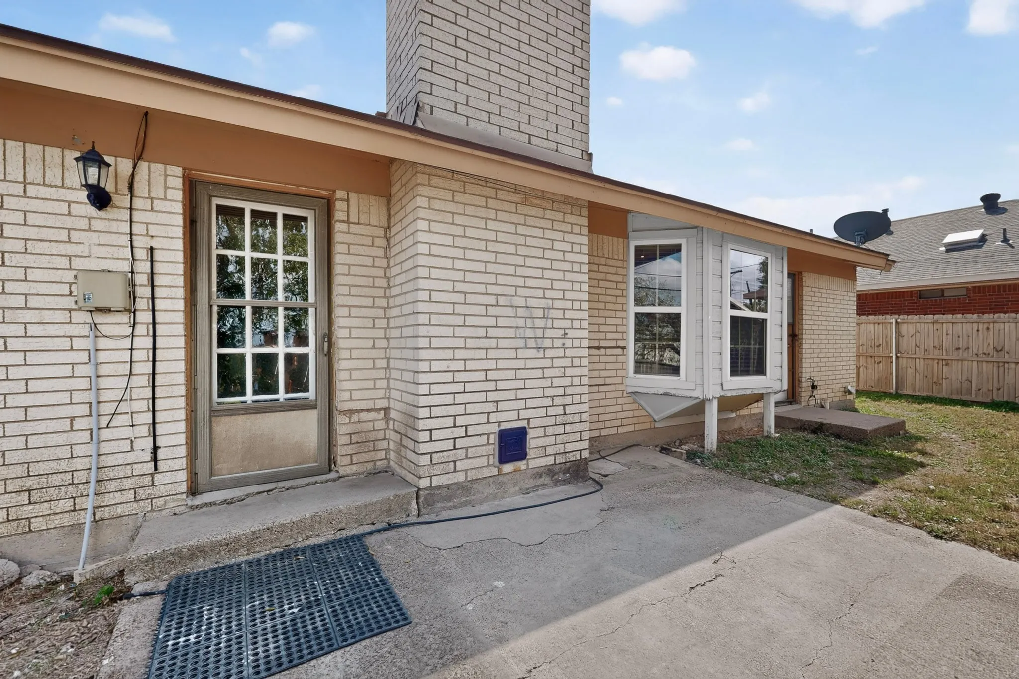Brick exterior featuring a masonry chimney, bay window, concrete patio, and grid-pattern glass entry door