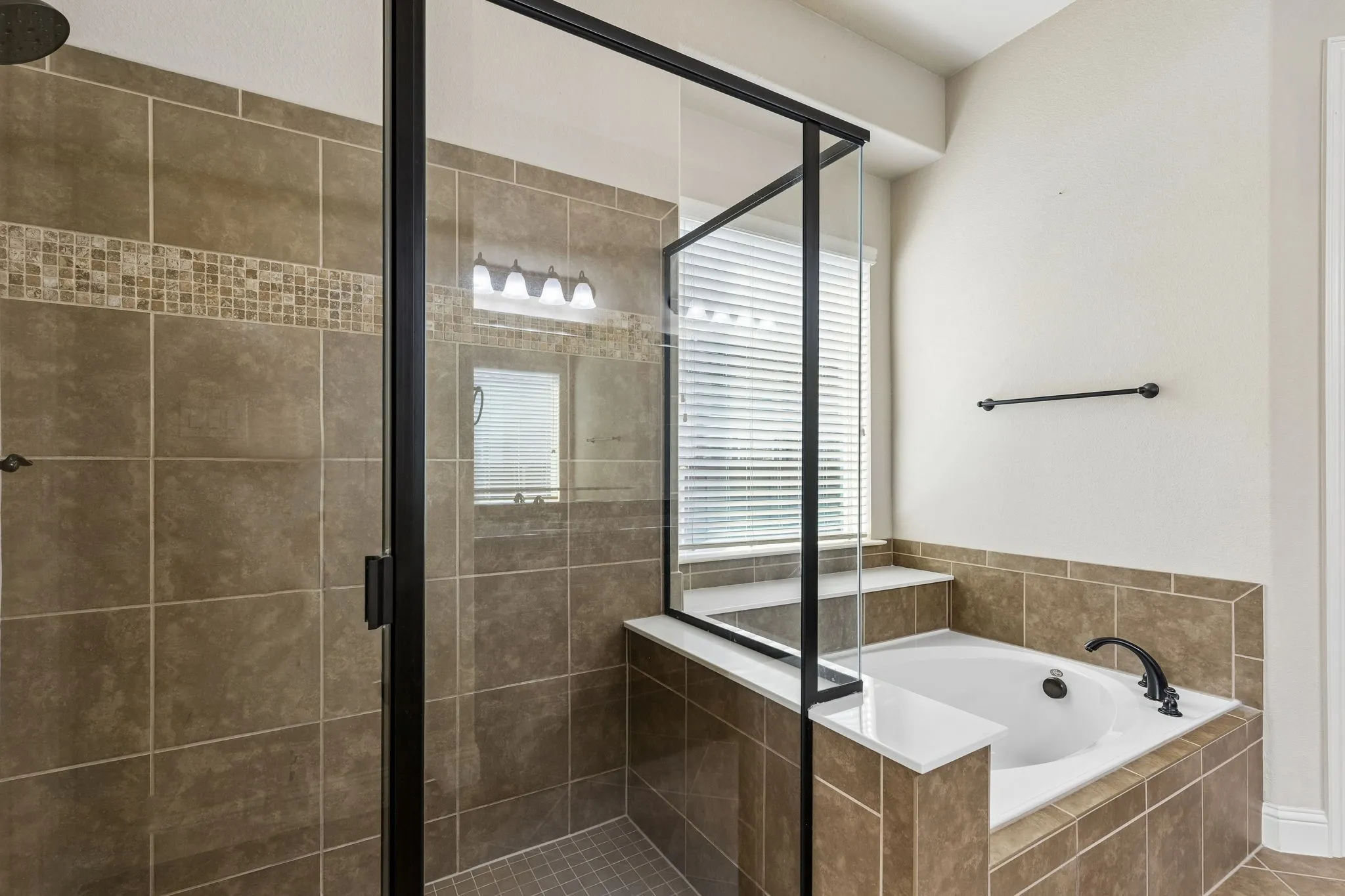 Walk-in shower with matte black frame and tile surround, built-in soaking tub with tile deck, and mosaic tile accent detailing