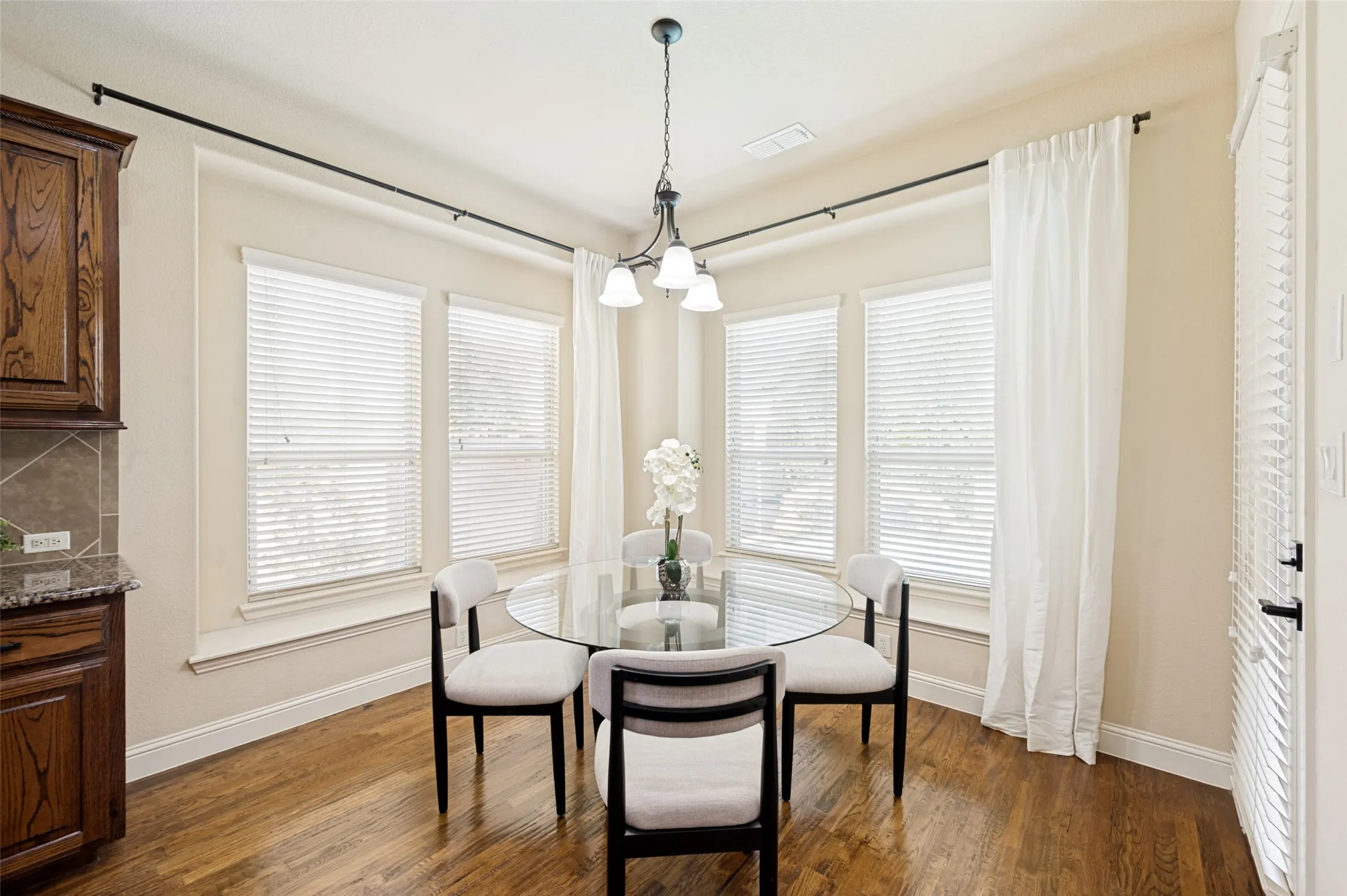 Corner area featuring wood-finish flooring, four multi-pane windows with horizontal blinds, and a three-light pendant fixture