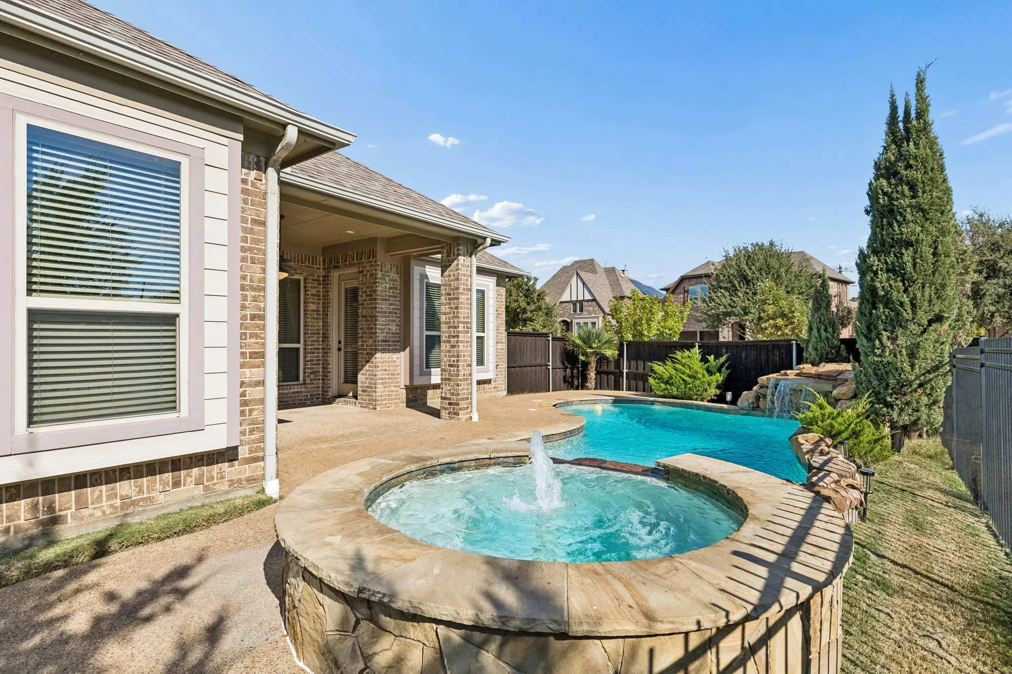 Brick and siding exterior featuring a covered patio, a stone-accented hot tub with a water feature, and a custom-shaped swimming pool