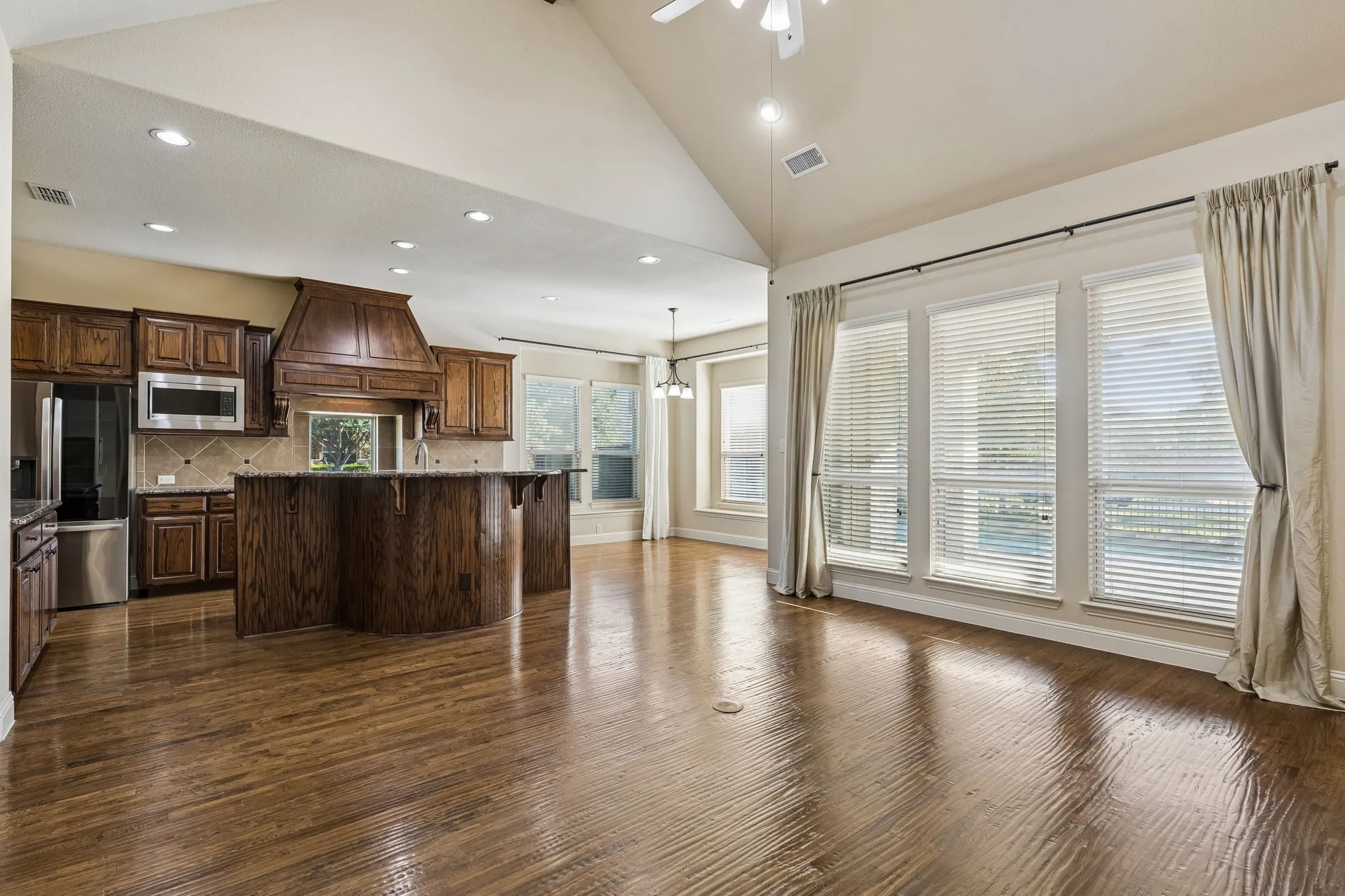 Vaulted ceiling, wood-finish flooring, custom wood cabinetry, central kitchen island, and expansive windows