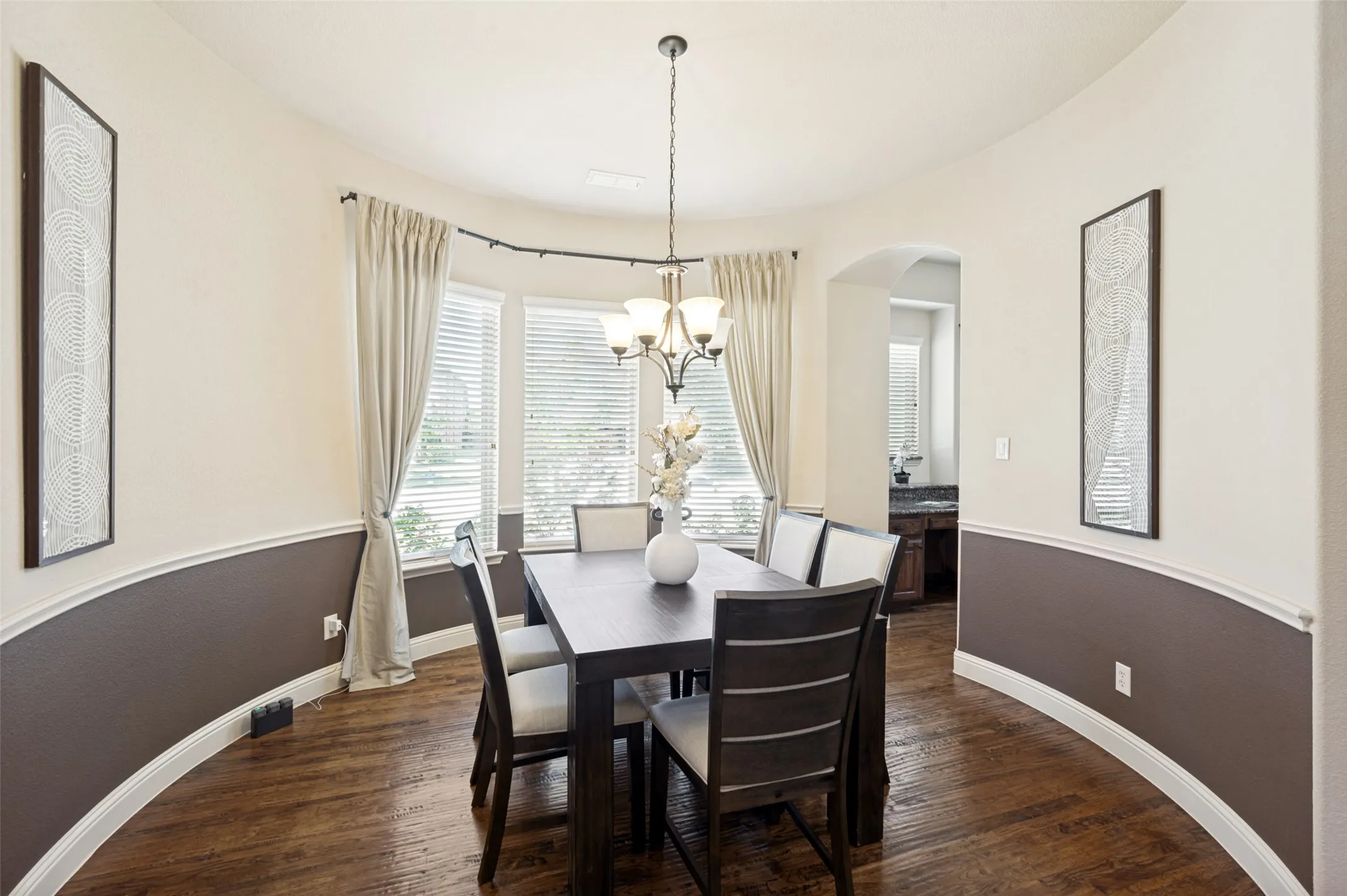 Curved wall design featuring two-tone paint, chair rail molding, wood-finish flooring, and a multi-light chandelier