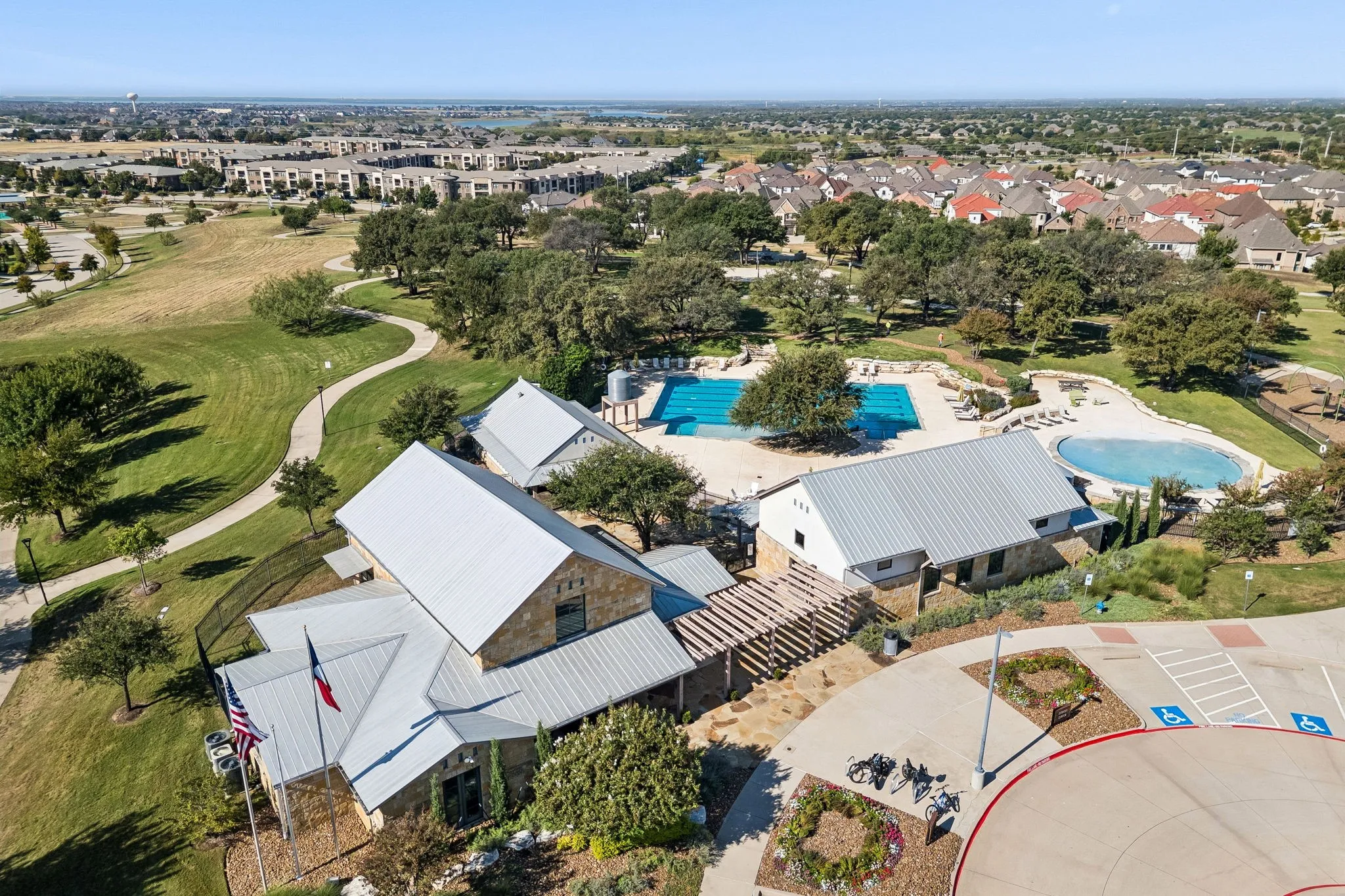 Community amenity complex featuring stone-exterior structures, metal roofing, dual outdoor swimming pools, and a wooden pergola