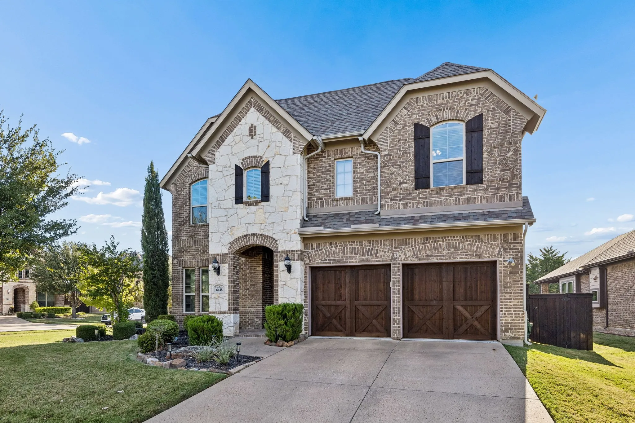 Two-story brick and stone facade featuring arched window detailing, dark-finished carriage-style garage doors, and decorative exterior shutters