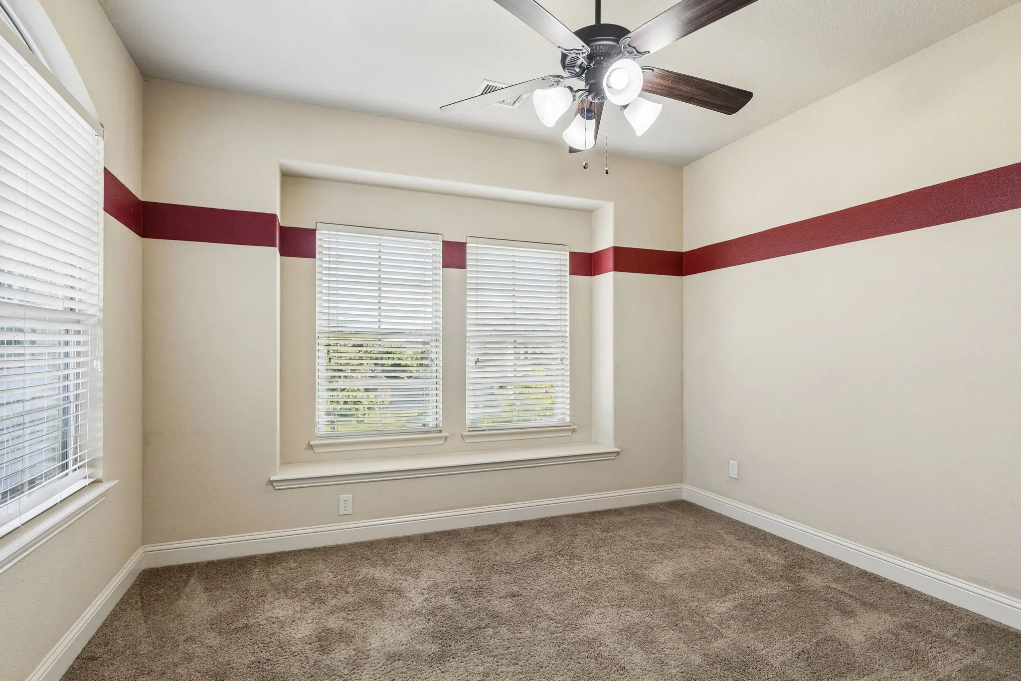 Recessed window nook featuring dual windows with horizontal blinds, neutral wall-to-wall carpeting, and a central ceiling fan with multi-light fixture
