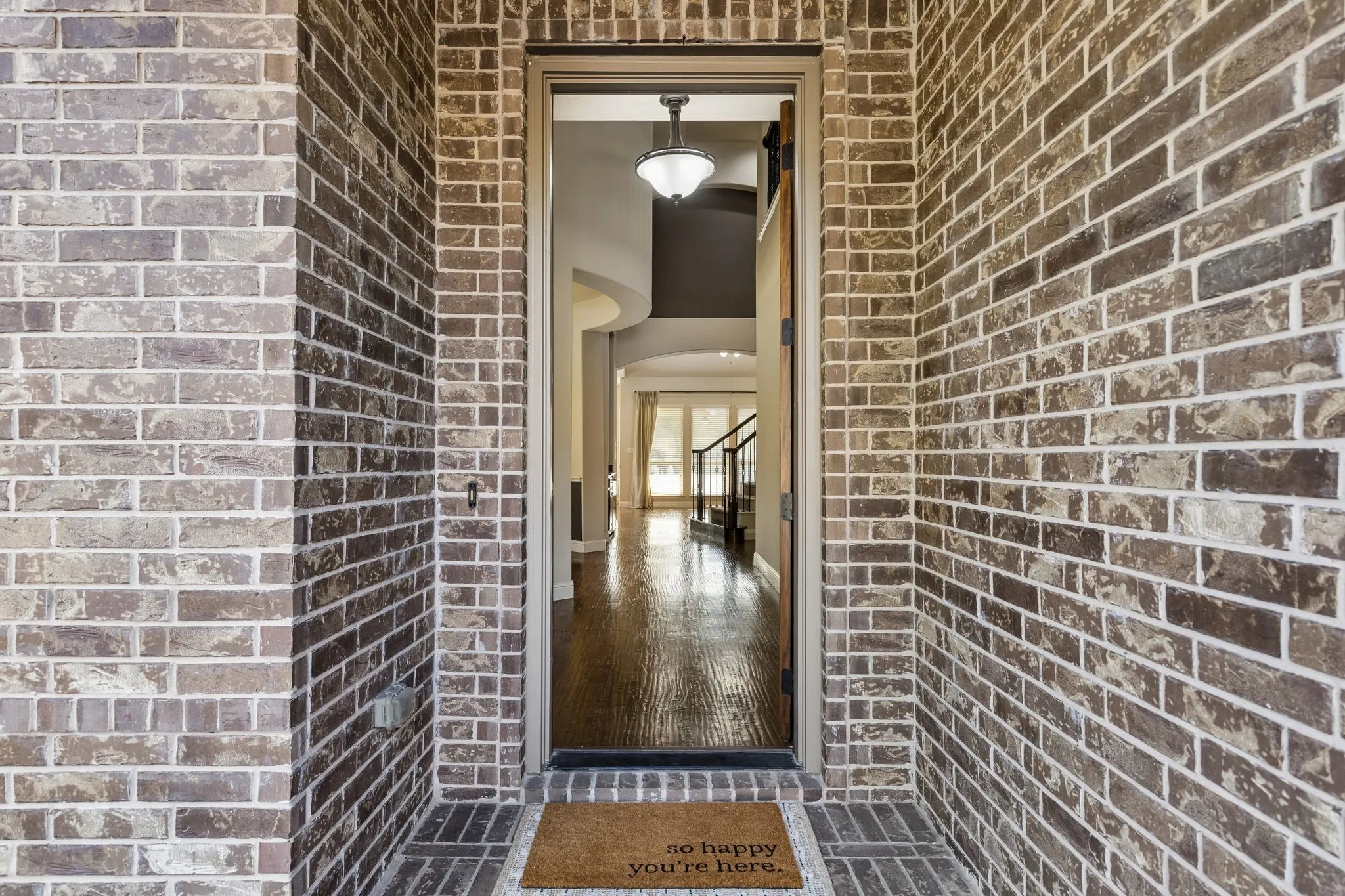 Exterior entrance featuring multi-tonal brick masonry, wood-finish flooring, and a pendant light fixture