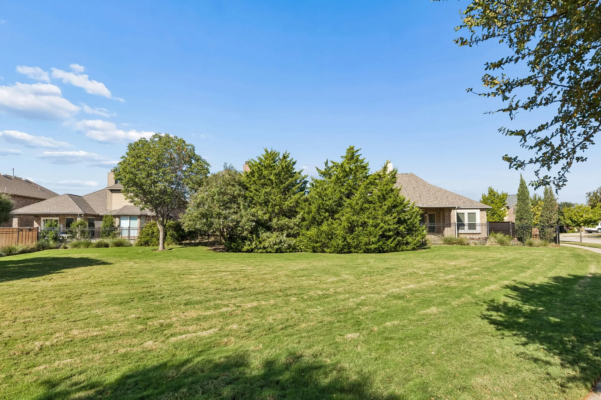 Expansive rear lawn featuring mature trees, manicured landscaping, and perimeter fencing