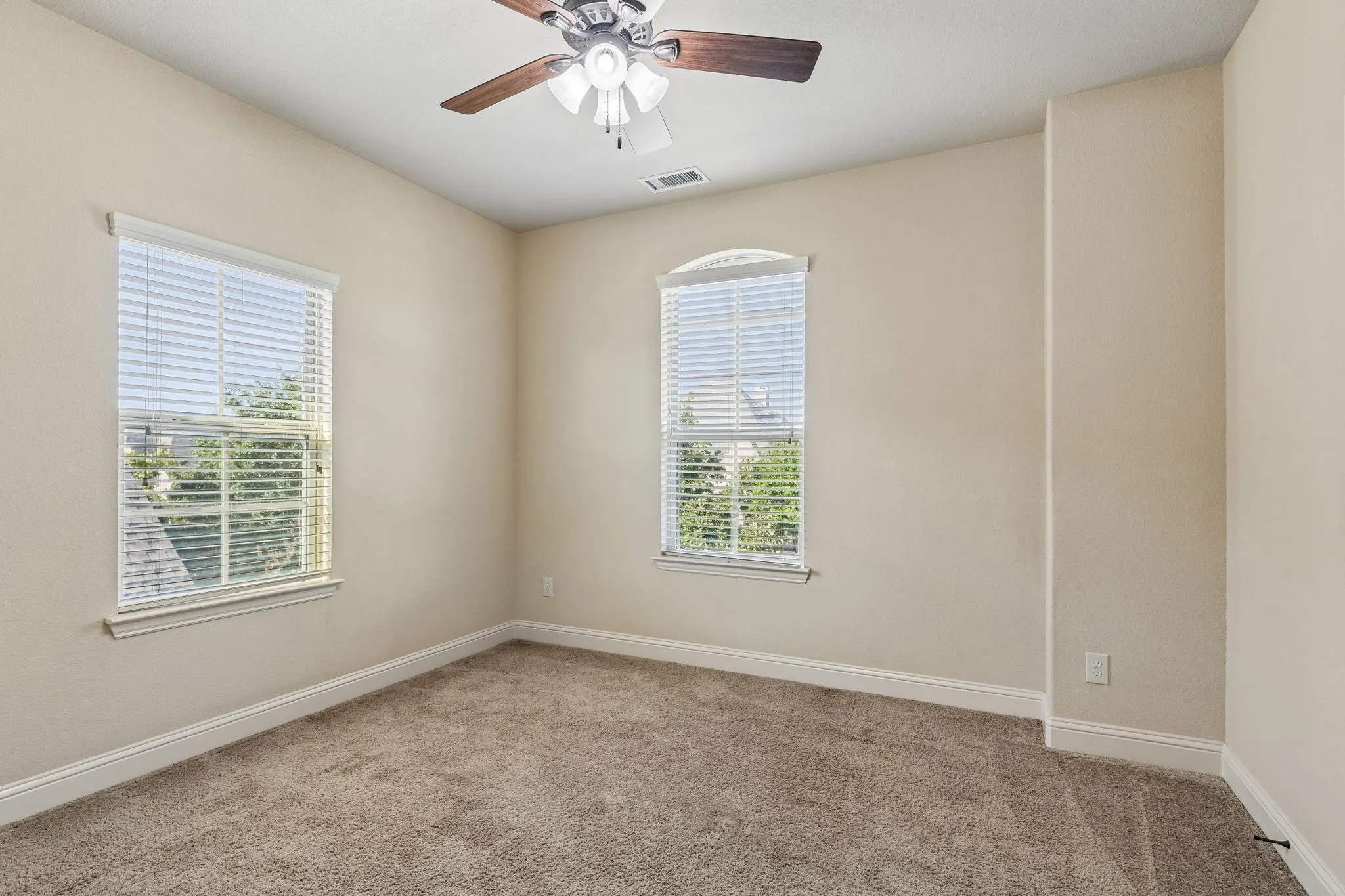 Interior space featuring neutral wall tones, carpeted flooring, two double-hung windows with arched upper panes, and a ceiling fan with integrated lighting