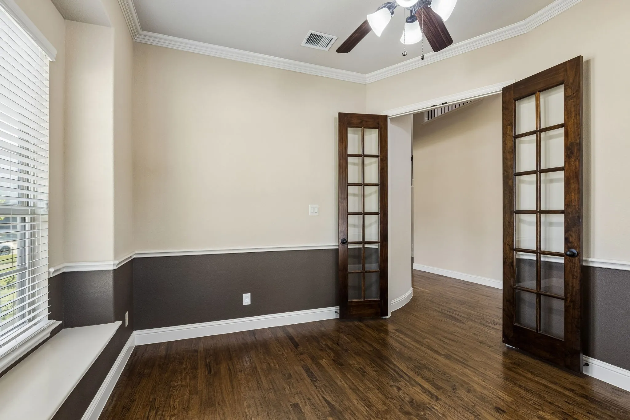 Room featuring wood-finish flooring, two-tone wall paint, built-in window seat, crown molding, and wooden French doors with glass panes