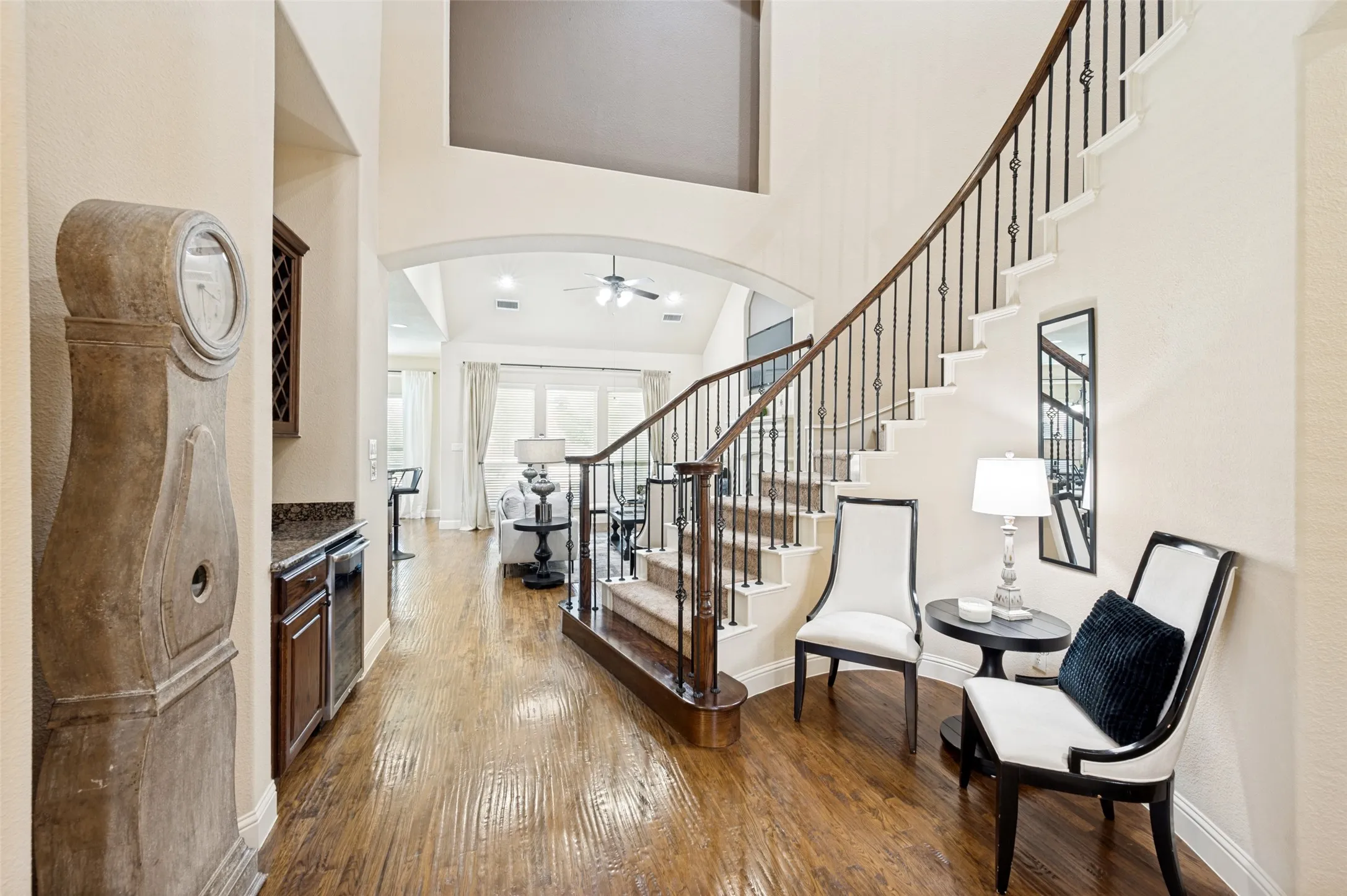 Grand foyer featuring soaring vaulted ceilings, wood-finish flooring, a built-in wet bar with dark cabinetry, and an ornate staircase with metal balusters