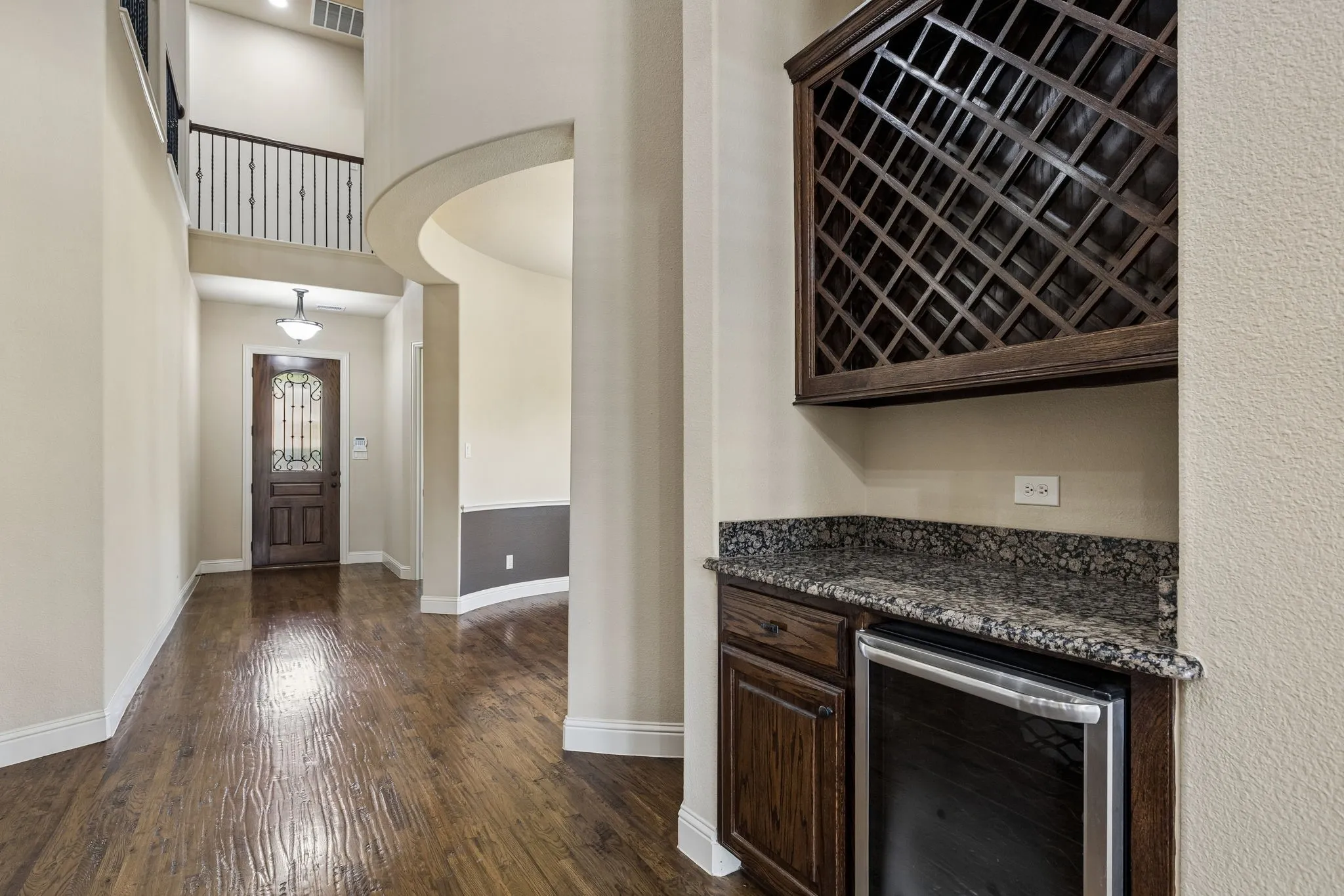 Built-in cabinetry featuring a stone-top counter, wine storage, and under-counter cooling unit, highlighted by wood-finish flooring, high ceilings, and metal stair railing