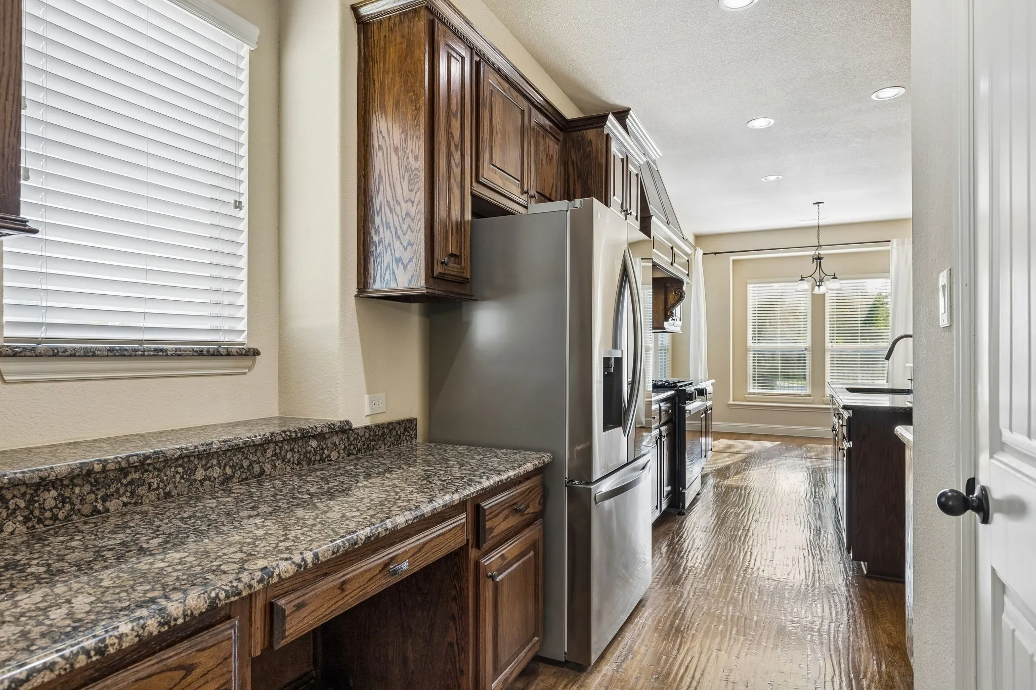 Kitchen area featuring wood-finish flooring, dark-stained cabinetry, stone countertops, and stainless steel appliances