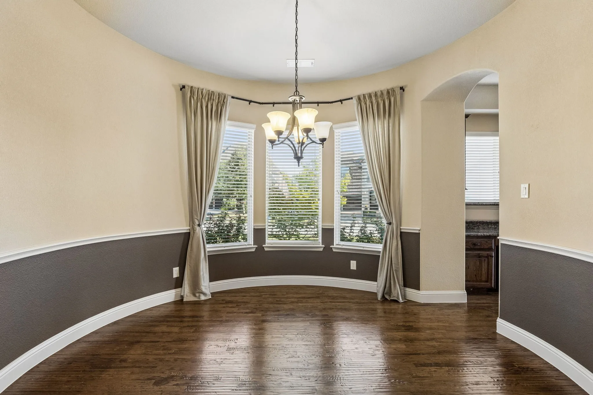 Curved wall detail featuring wood-finish flooring, two-tone wall paint, decorative chair rail molding, and a multi-light chandelier