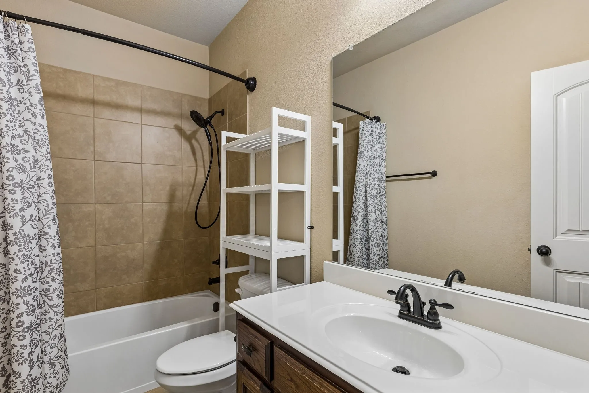 Bathroom featuring a vanity with a white countertop and oval under-mount sink, dark wood-finish cabinetry, matte black hardware, and a shower-tub combination with tiled surround