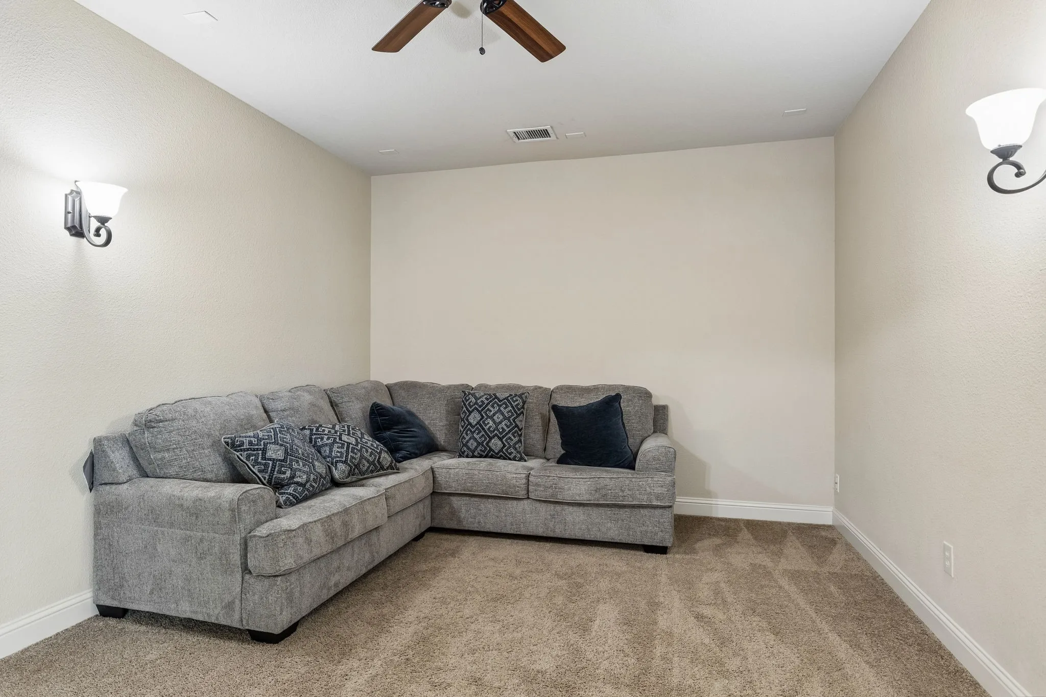 Neutral wall tones, plush wall-to-wall carpeting, ceiling fan with light fixture, and dual wall-mounted sconces