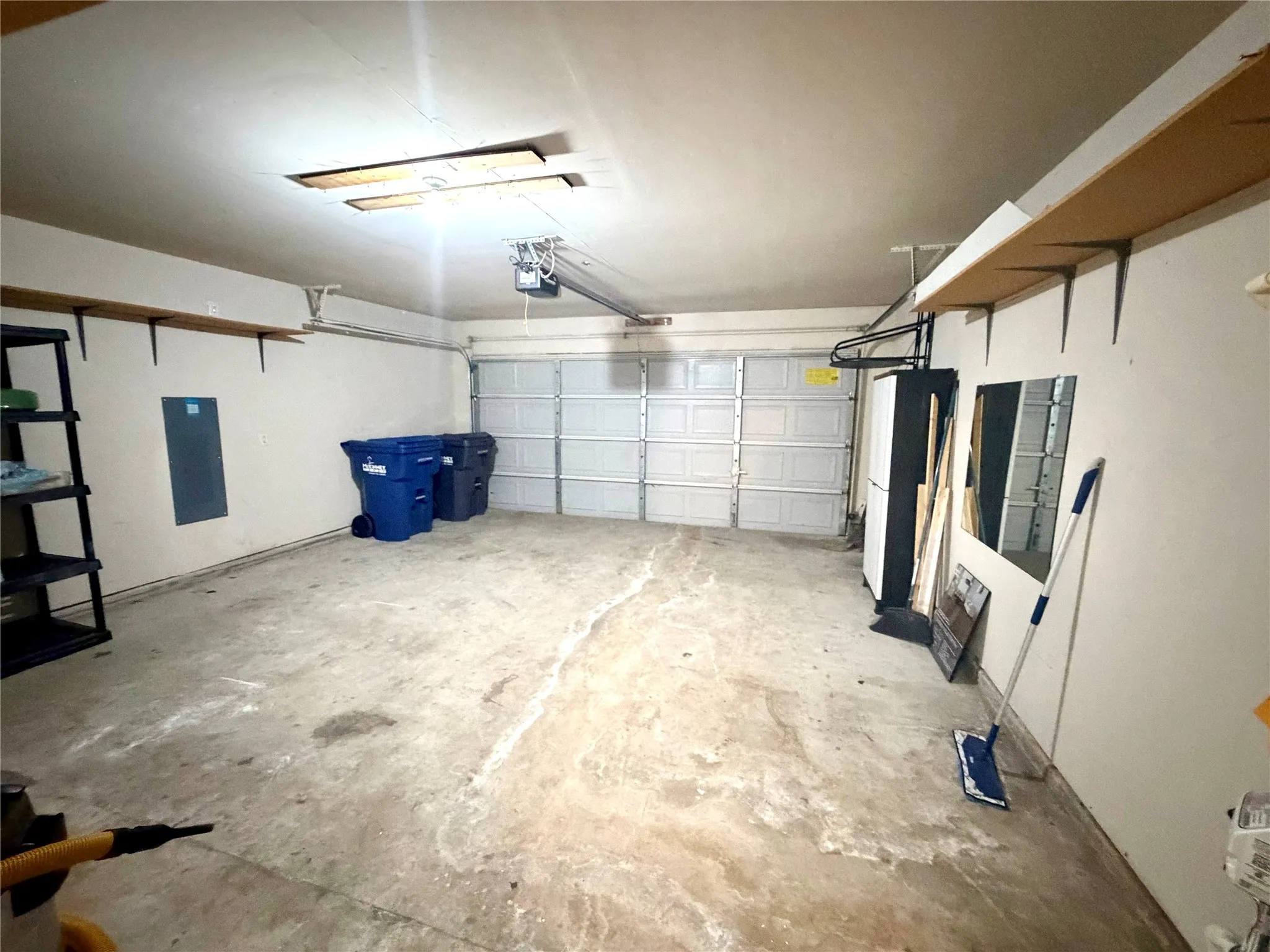 Attached two-car garage featuring a sectional door, concrete flooring, and perimeter wall-mounted shelving