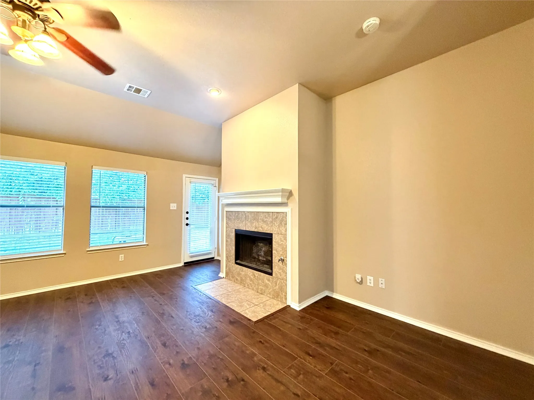 Vaulted ceiling with a central paddle fan, wood-finish flooring, and a fireplace featuring a tile surround and a crown-molding mantle