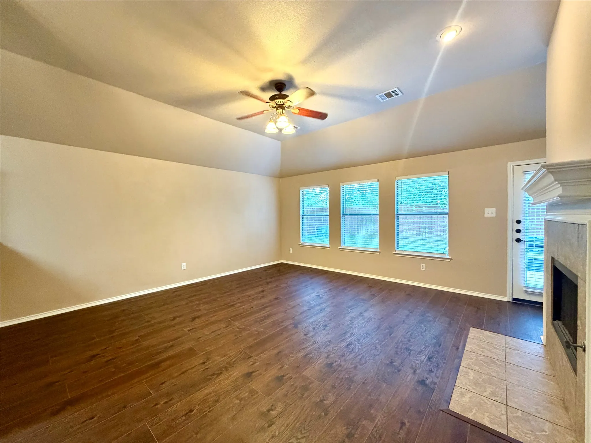 Vaulted ceiling, wood-finish flooring, recessed lighting, ceiling fan with light kit, and a stone-surround fireplace with a mantel