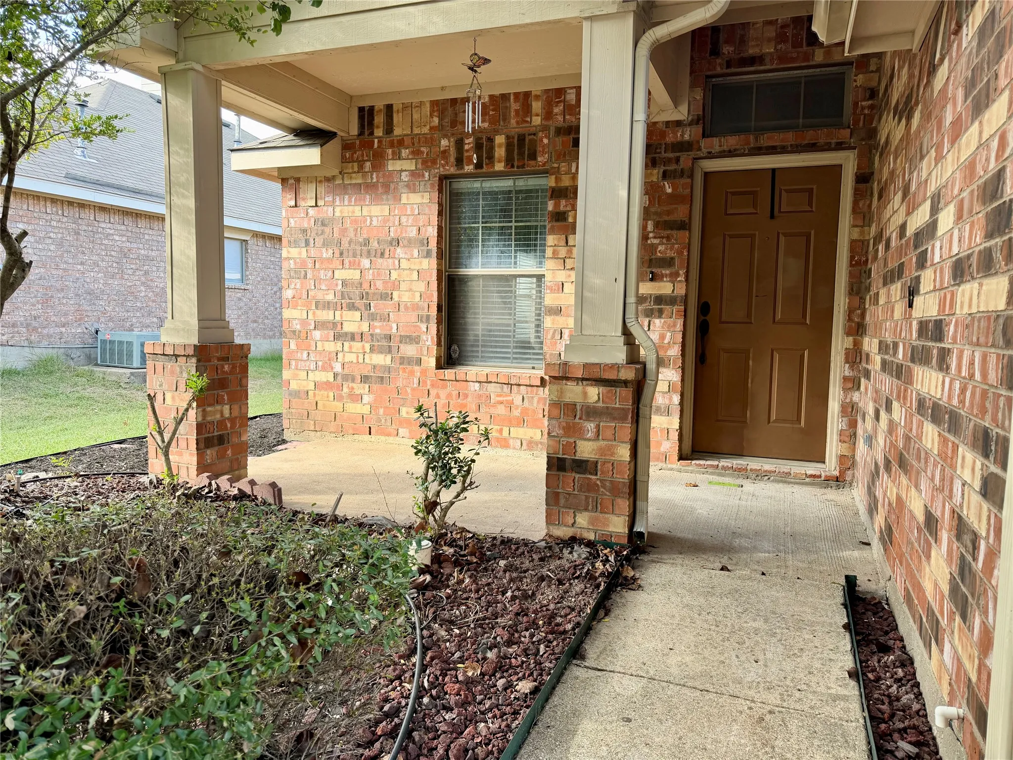 This photograph features the charming brick exterior of the property, highlighting a welcoming covered front porch, and a sturdy solid-panel front door enhanced by an attractive integrated transom window that allows for natural light.